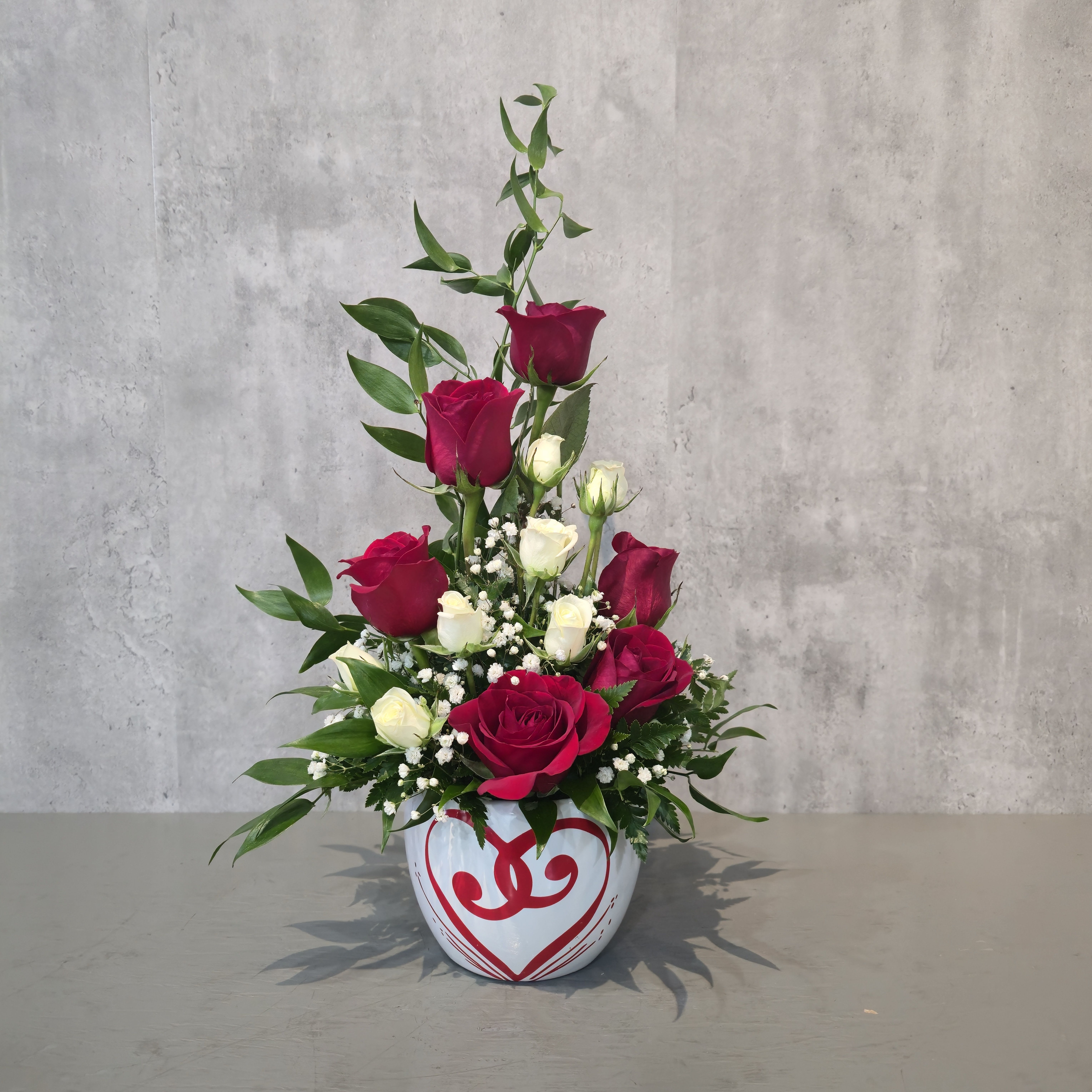 Half Pint Roses - Sweet, charming, and full of romance, Half Pint Roses is a beautifully designed petite rose arrangement perfect for meaningful moments. Featuring rich red roses, delicate cream spray roses, soft baby’s breath, and fresh seasonal greenery, this bouquet is arranged in a festive Valentine keepsake container.  Ideal for Valentine’s Day, anniversaries, birthdays, and “just because” gifts, this compact design fits perfectly on desks, nightstands, and small spaces while making a big impression.  Handcrafted to order by a local Albuquerque florist, Half Pint Roses is a thoughtful choice for anyone searching for fresh rose delivery in Albuquerque, romantic flower arrangements, and Valentine’s flowers near me.  Available for flower delivery throughout Albuquerque, NM.