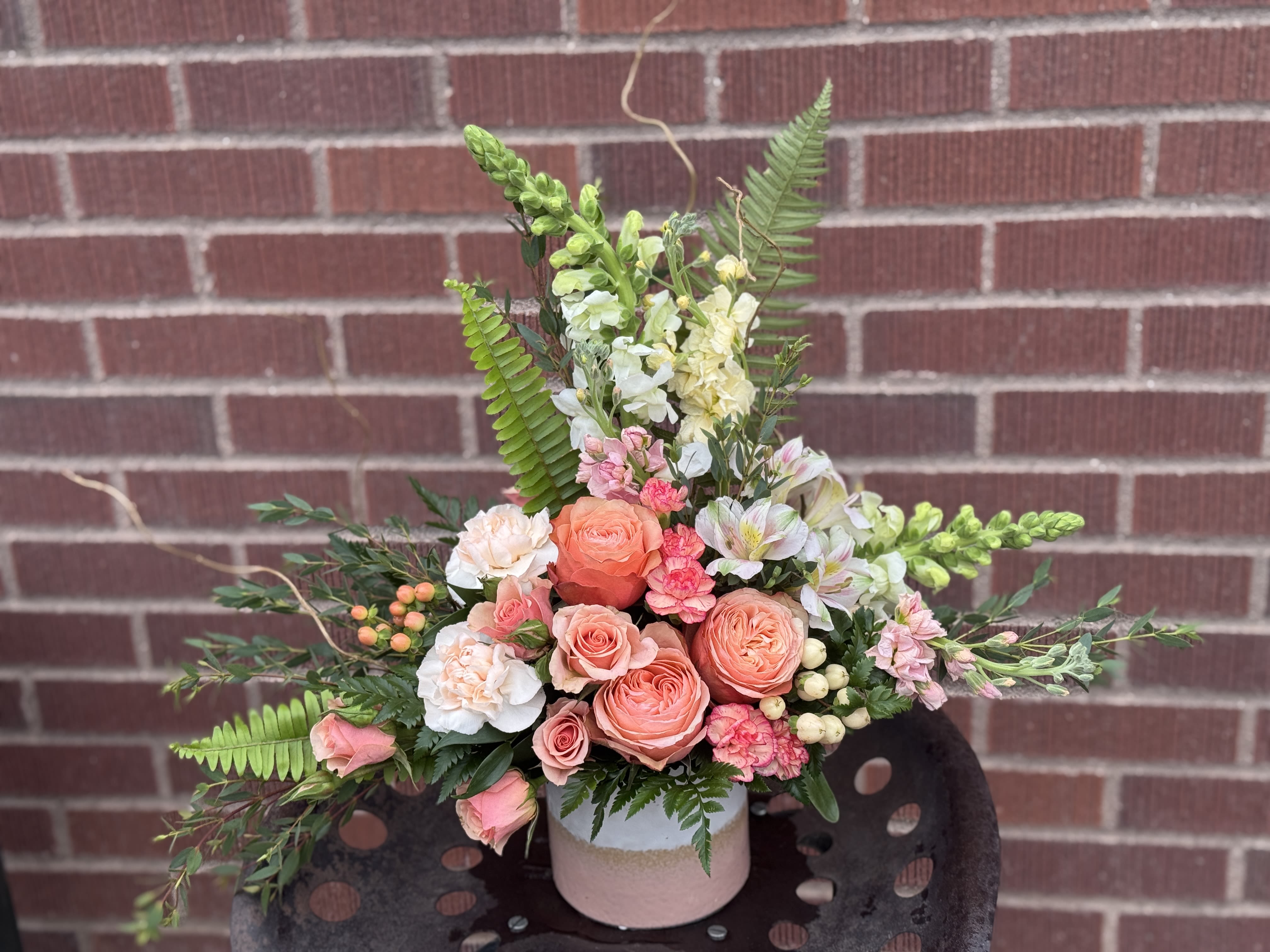 Peach and pink floral arrangement in a pink vase with fern accents