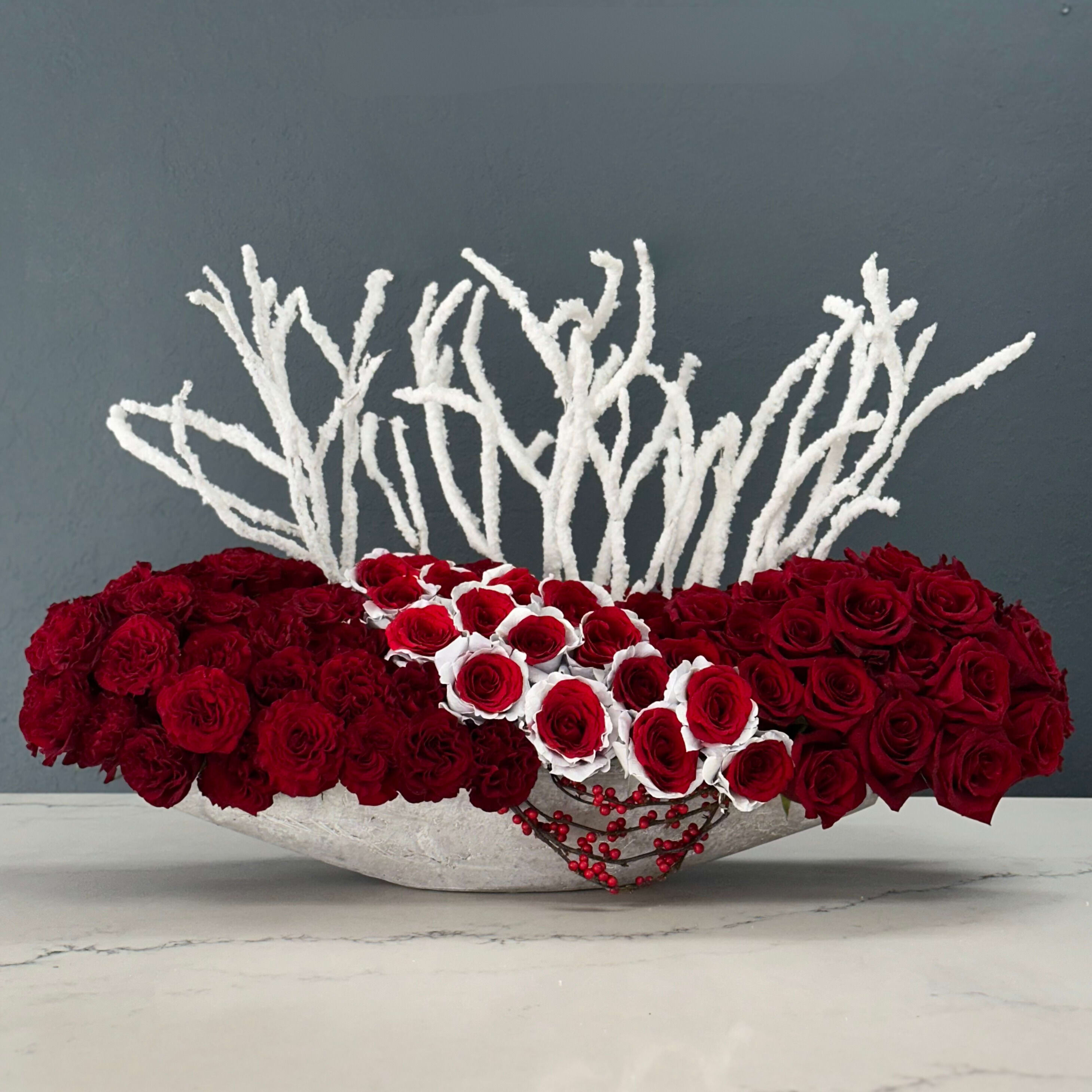 Berry Bliss - A special Christmas masterpiece that marries the timeless allure of deep red roses with the industrial elegance of a long, sleek cement vase. This stunning arrangement embodies the spirit of the season, combining the passion of red roses with the understated beauty of its vessel.