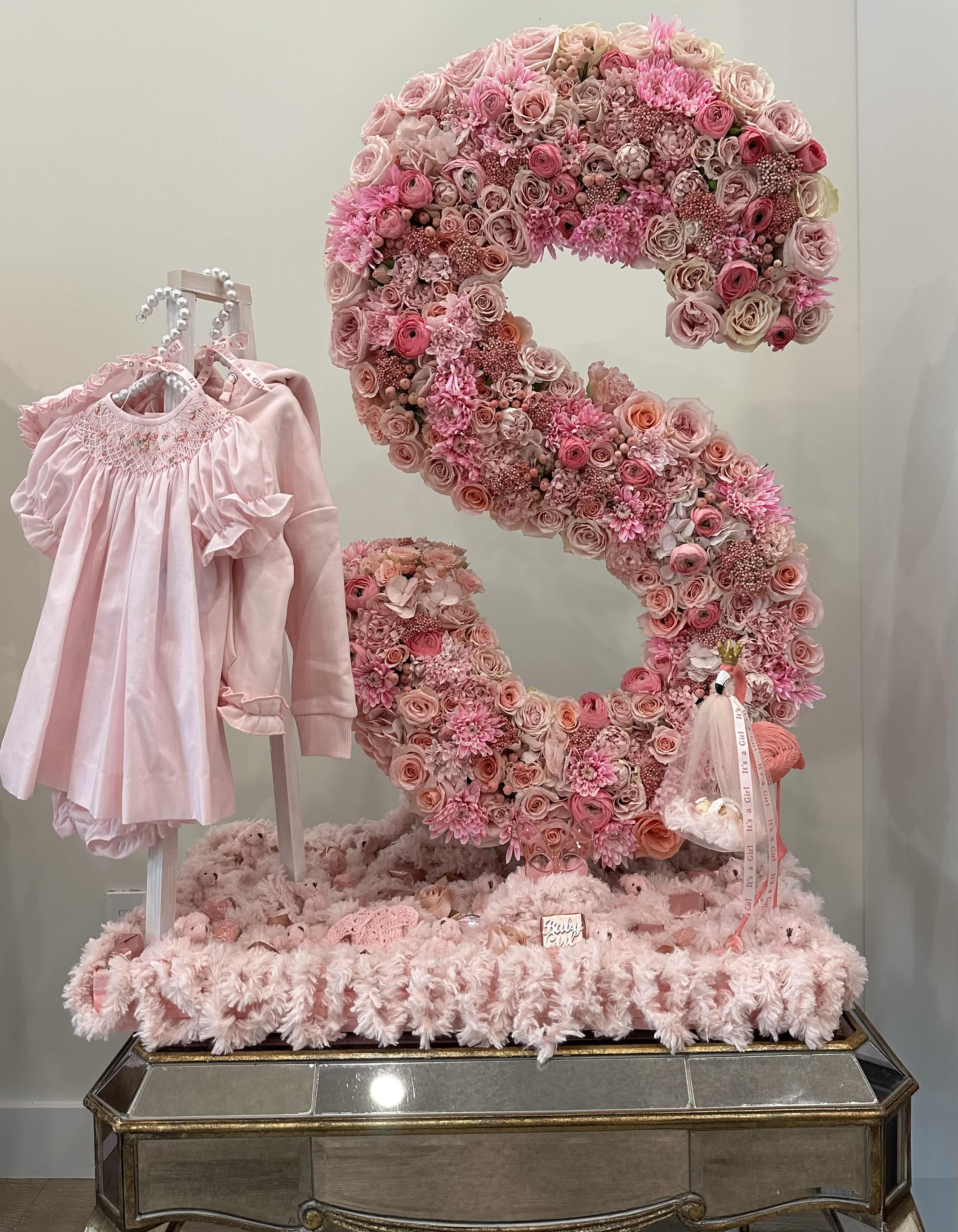 Pink Petal Baby Letter - Welcoming a baby to the world is truly a blessing and needs to be celebrated big. This massive floral tray consists of a huge letter resembling the baby's first initial, with a mini gift closet placed neatly to its right. The tray consists of a specialty arrangement with unique flowers. The letter "S" consists of mainly roses, topped off with anemone and ranunculus.  Dimensions: 45" long with the Letter standing 40" tall.  NOTE: The letter of choice must be noted upon order being placed. If there needs to be any changes made to the look of the tray, such as placements, size adjustments, and color schemes, please call (747)-441-9479.  