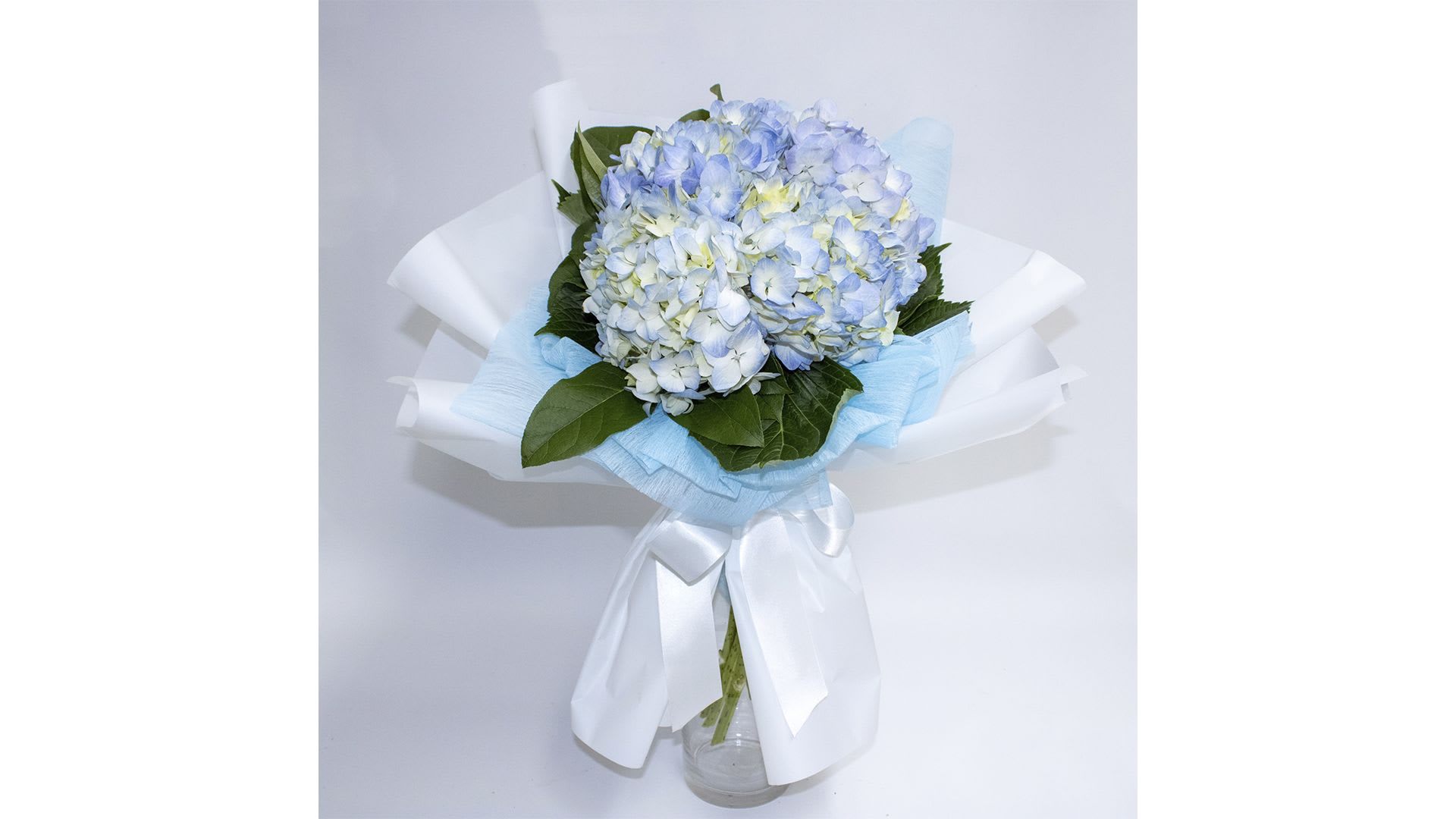 Blue and white hydrangea bouquet wrapped in white paper with a ribbon