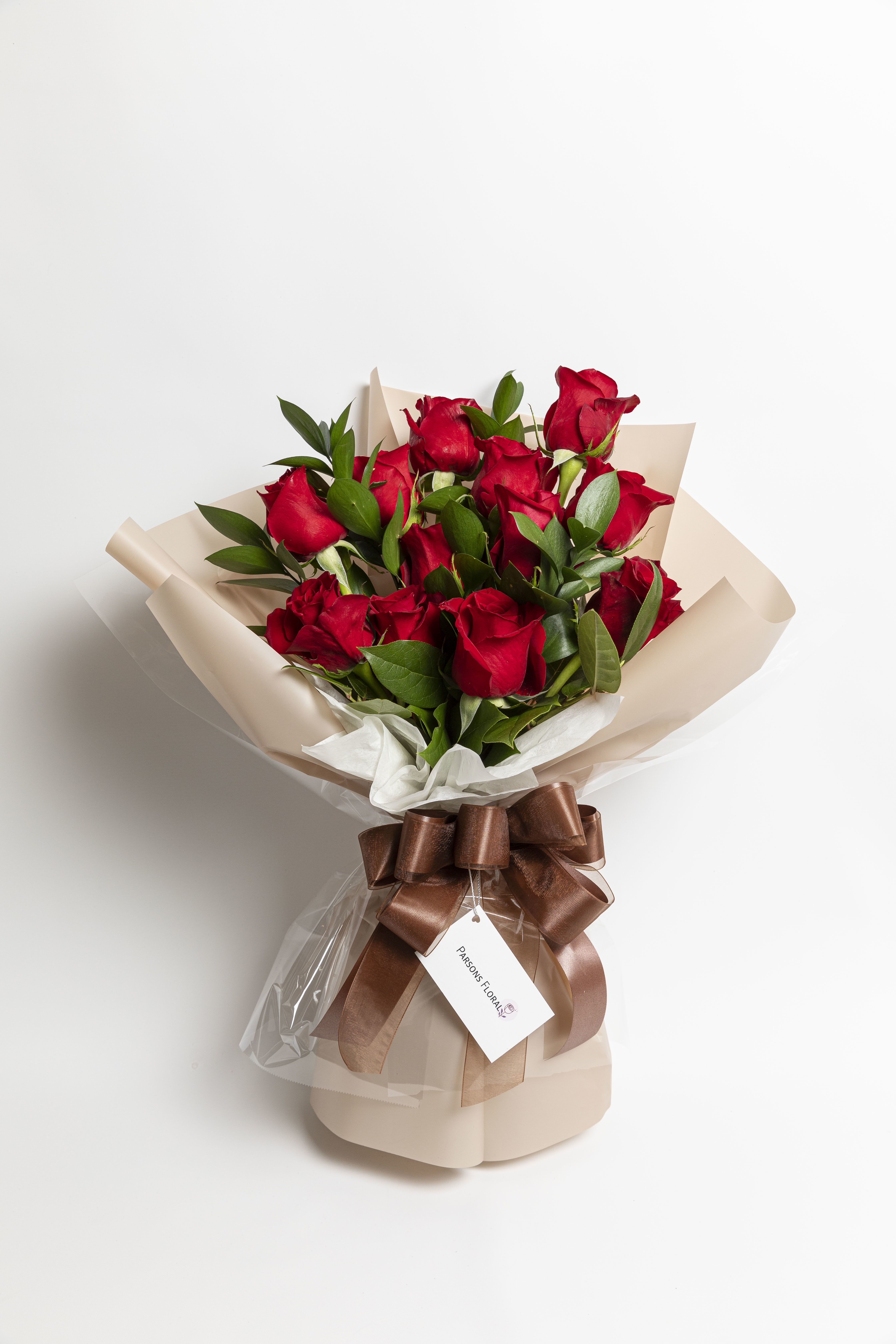 Bouquet of red roses wrapped in beige paper with a brown ribbon