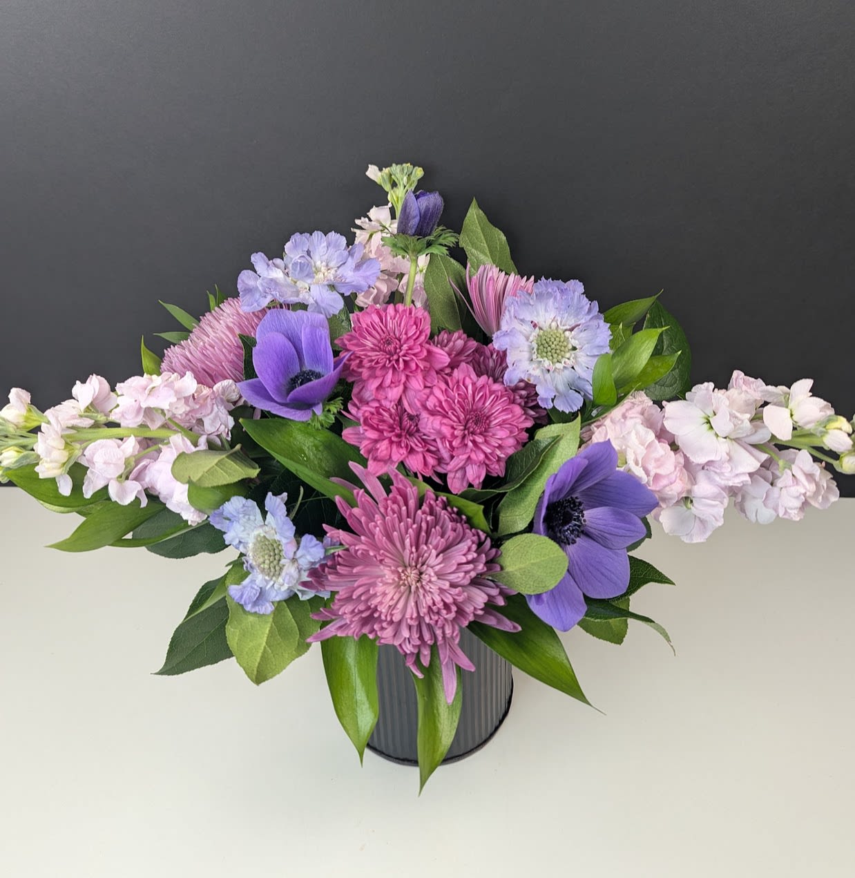 Lavender Mist Bouquet - Drift into Tranquility with the Lavender Mist Bouquet  Soft and serene, the Lavender Mist Bouquet evokes the beauty of a gentle morning haze with its delicate blend of cool and pastel tones. This enchanting arrangement features:  -Purple mums -Pastel pink stock -Light blue scabiosa -Purple anemones  Perfect for bringing a sense of calm and elegance to any space, this bouquet is a lovely choice for gifts, celebrations, or simply indulging in a moment of floral beauty.  