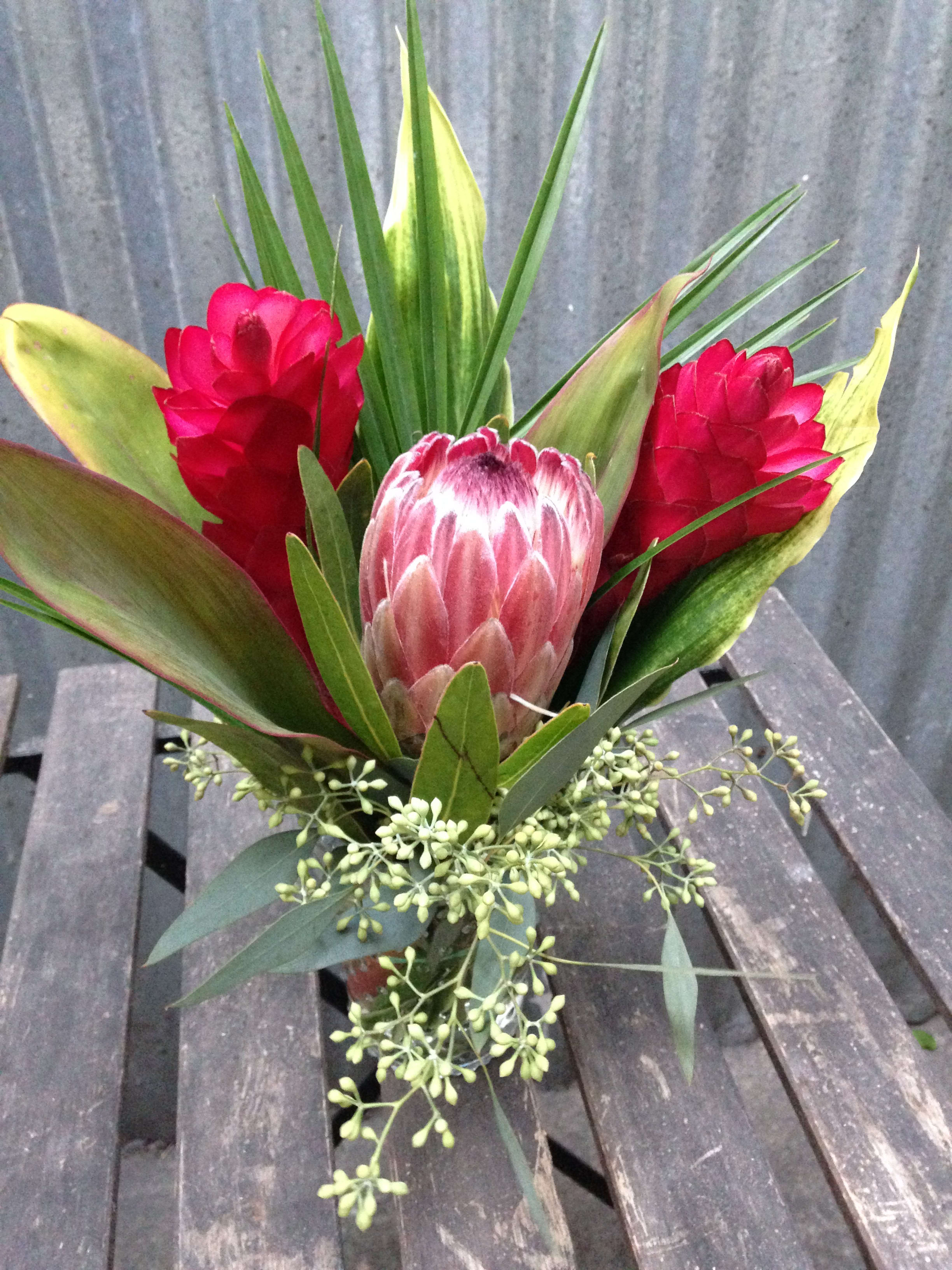 A Trip to the Tropics Jar. [Pre-order] - This mason jar is full of tropical vibes to liven up someone's day! Featuring protea and tropical greenery. (Some flowers may be subject to change depending on the season. We will contact you with available flower substitutions; please contact us with specific questions if you are concerned with flower availability, thanks!) Featured Arrangement: $78.00 [PRE-ORDER ]