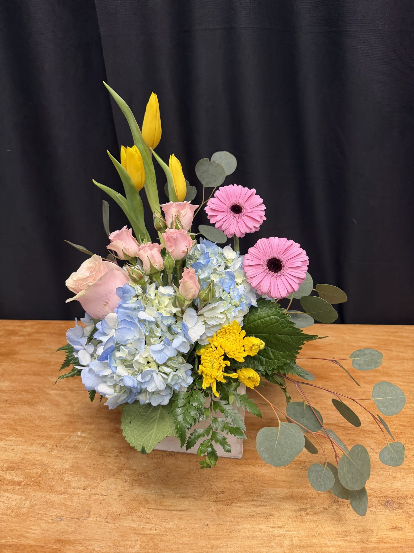 Pastel Garden Delight - Pastel Garden Delight is a soft and cheerful arrangement featuring delicate pink roses, airy blue hydrangea, bright gerbera daisies, and sunny yellow tulips. Accented with fresh greenery and seasonal blooms, it brings a light, garden-inspired elegance to any space. This charming design is perfect for celebrating birthdays, welcoming spring, or simply brightening someone’s day.