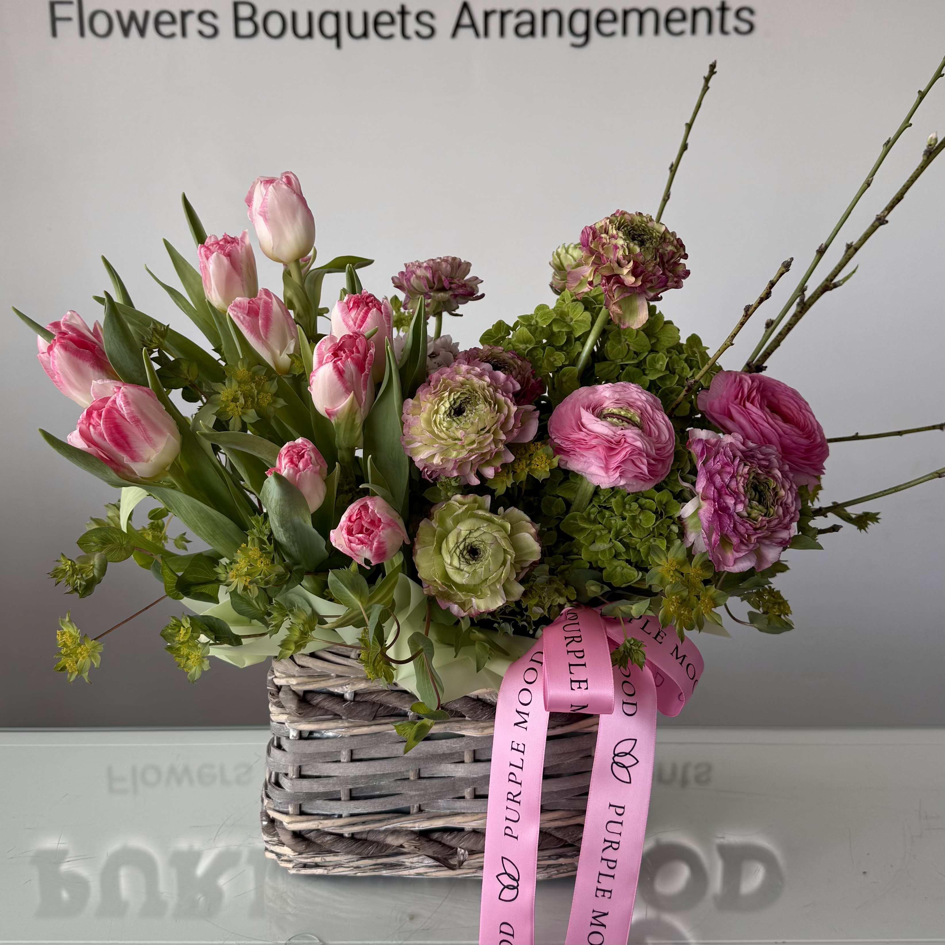 Tulips &amp; Ranunculus Basket - A charming spring arrangement featuring fresh yellow tulips and delicate ranunculus, beautifully complemented with seasonal blooms and soft greenery. Designed in an elegant mini basket, this arrangement brings a bright, fresh touch of spring to any space.  Perfect for celebrating a special moment, sending a cheerful surprise, or simply brightening someone’s day.