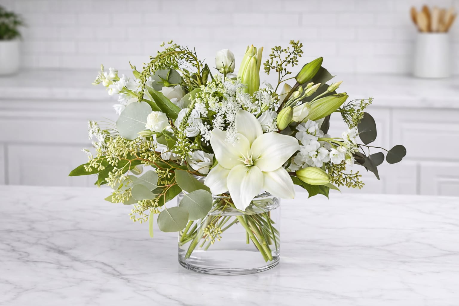 Enchanting Arrangement - This striking array of ivory and green within a clear glass vase. Handcrafted using Asiatic lilies interwoven with, white stock, and silver dollar eucalyptus and seeded eucalyptus, this bouquet graces every room with a touch of elegance.  