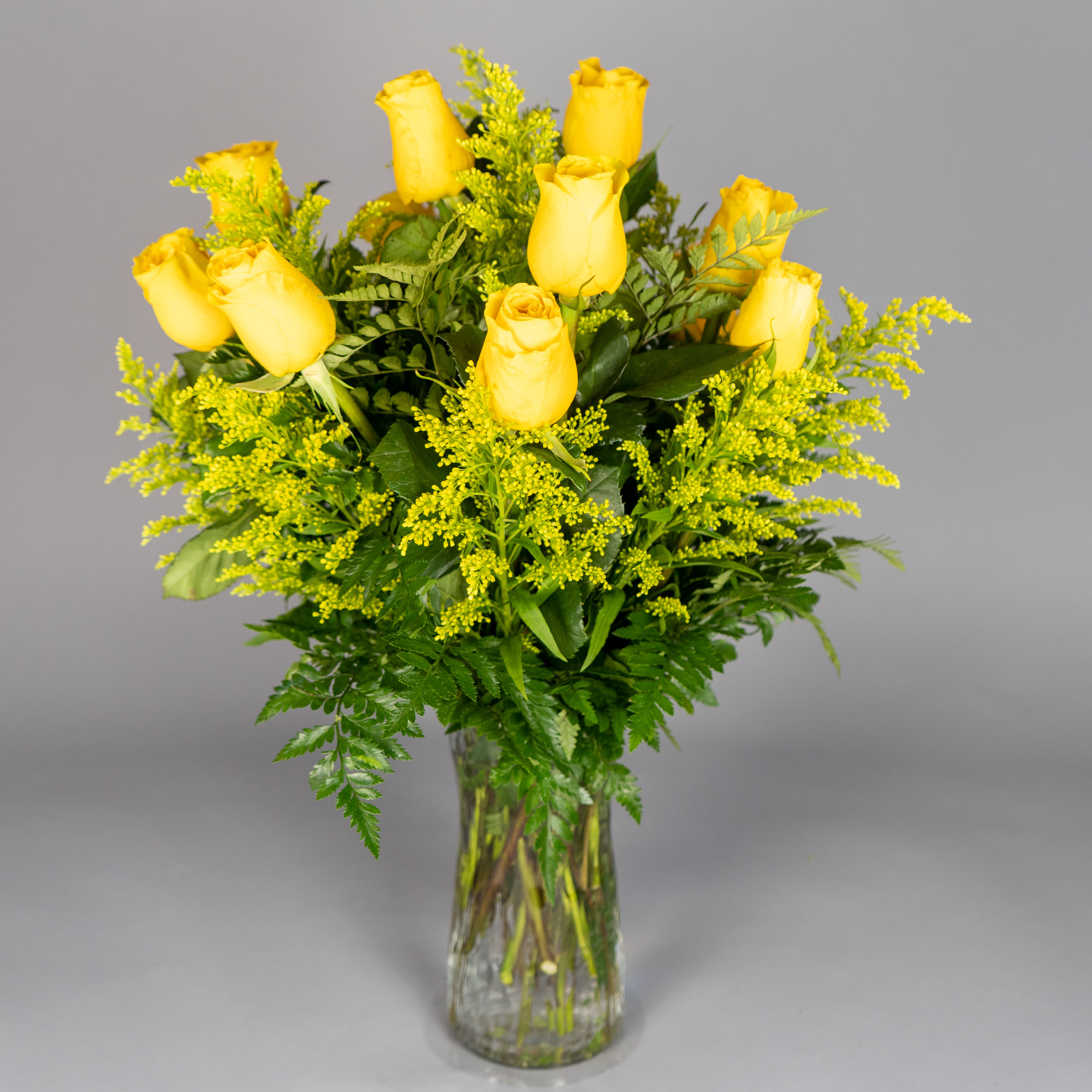 Arrangement of yellow roses with yellow filler in a clear glass vase
