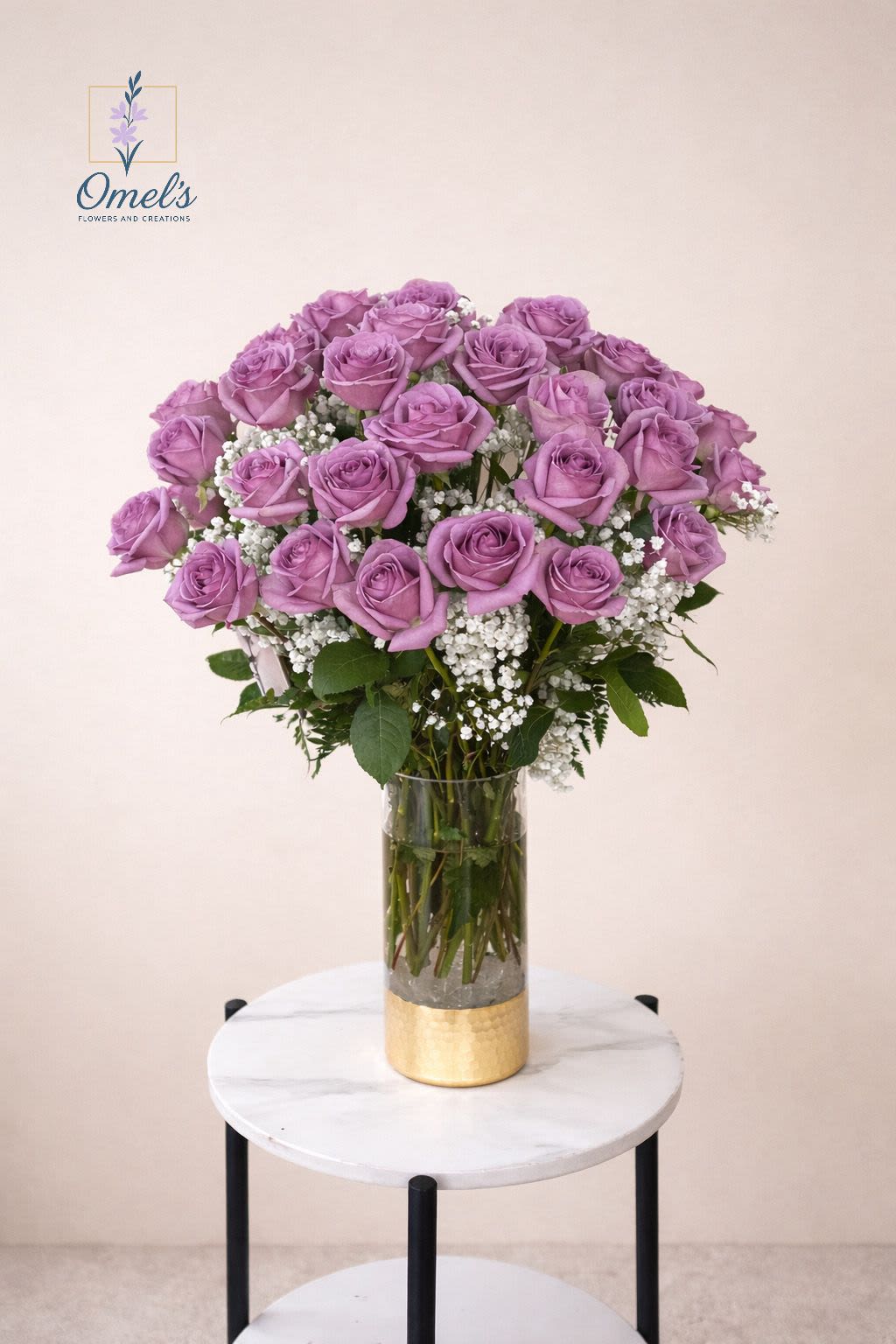 25 Lavender Roses - Soft, romantic, and effortlessly elegant   This Valentine’s Day arrangement features a lush gathering of lavender roses, their velvety petals symbolizing enchantment and love at first sight. Each bloom is thoughtfully accented with delicate clouds of baby’s breath, adding a light, dreamy touch that enhances the roses’ natural beauty. Arranged in a modern clear glass vase with a warm gold base, the design feels both timeless and elevated—perfect for making a heartfelt statement.  Whether you’re celebrating a great love, a new romance, or simply reminding someone how cherished they are, this arrangement speaks volumes without saying a word. It’s graceful, luxurious, and undeniably romantic—just like Valentine’s Day should be.  