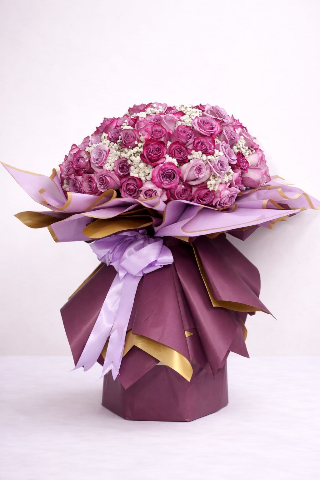 25 Roses Lavender &amp;  Purple Wrap - Twenty-Five Lavender and Purple roses in a classic wrap using the same colors with a hint of gold. Add chocolates, a balloon, or a teddy bear while supplies last.