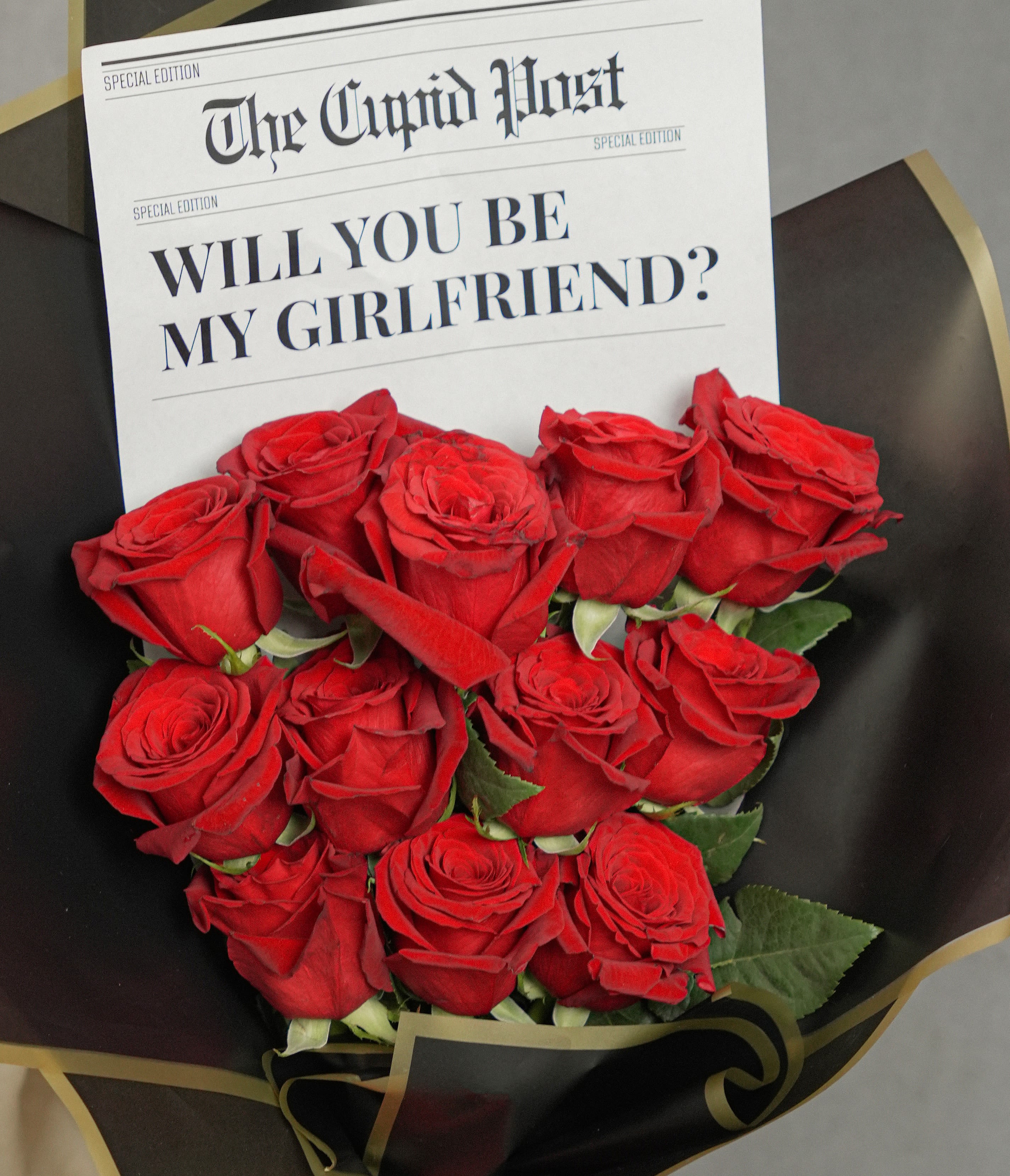 WILL YOU BE MY GIRLFRIEND 12 ROSES  - Striking bouquet featuring 12 premium red roses, imported from Ecuador, wrapped in sleek black Korean paper . Includes a newspaper-style note printed with the message “Will you be my Girlfriend”, adding a modern and romantic touch—perfect for making a bold love statement.