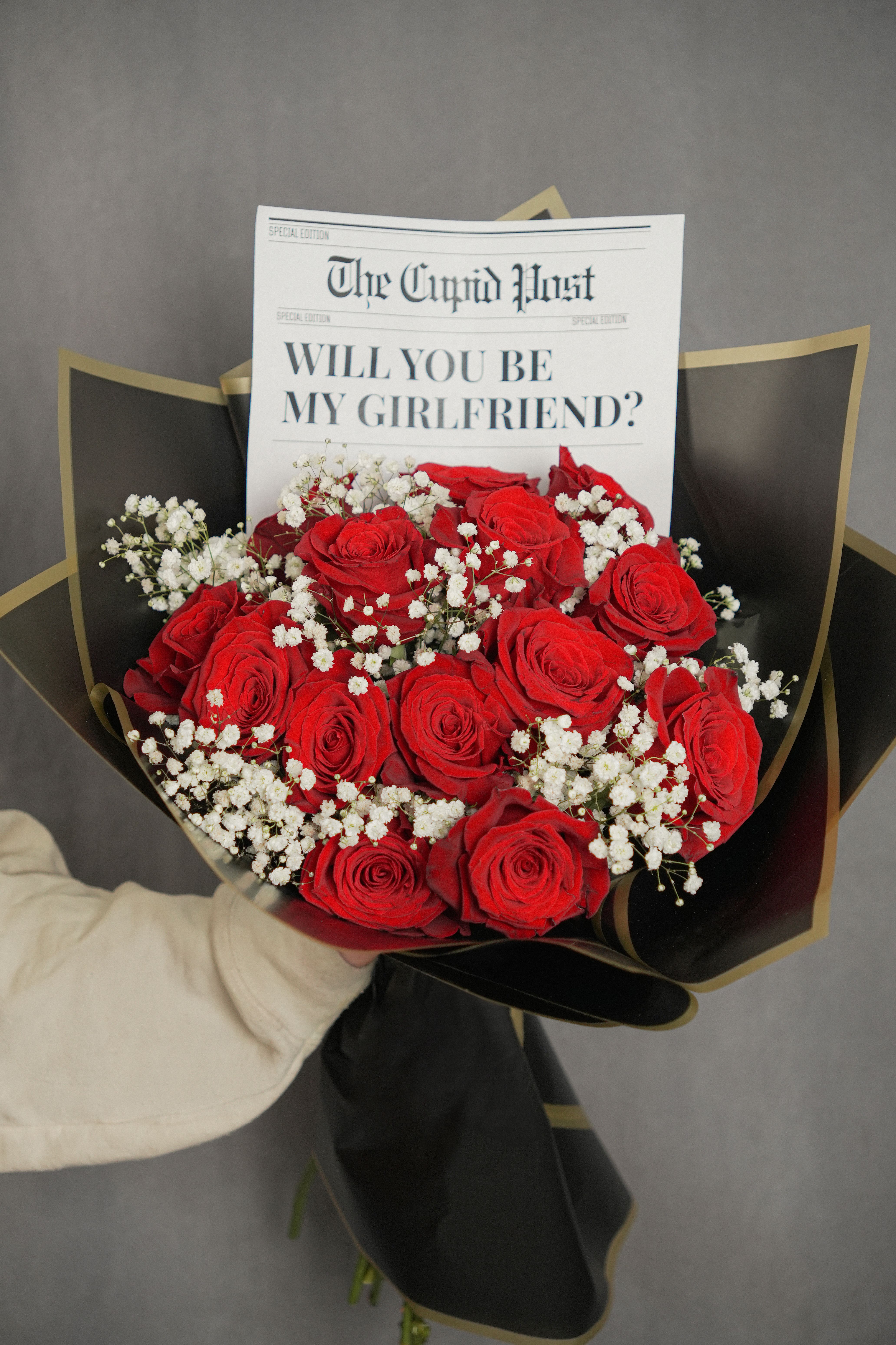 WILL YOU BE MY GRILFRIEND BOUQUET - Striking bouquet featuring 12 premium red roses, imported from Ecuador, wrapped in sleek black Korean paper and delicately accented with baby’s breath. Includes a newspaper-style note printed with the message “Will you be my Girlfriend”, adding a modern and romantic touch—perfect for making a bold love statement.