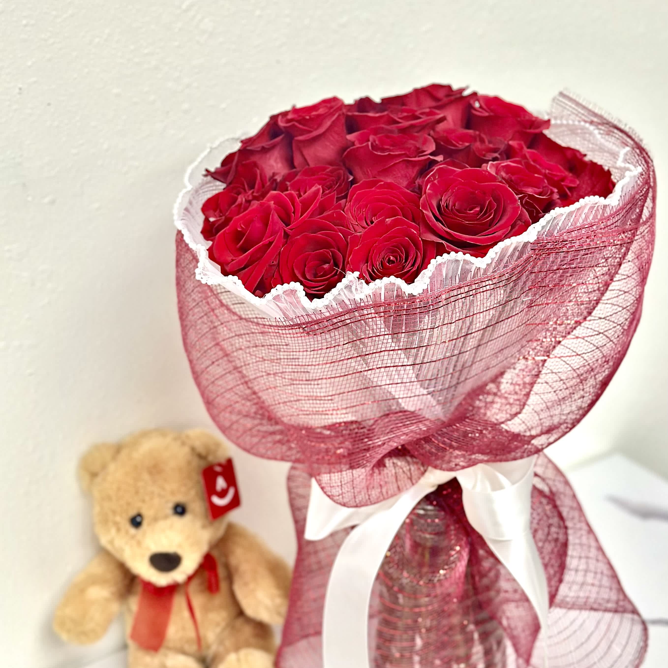 Coquette in Red  - A round bouquet of roses wrapped in pink paper, accented with pearl-decorated paper.  Flower types may vary depending on the season. 