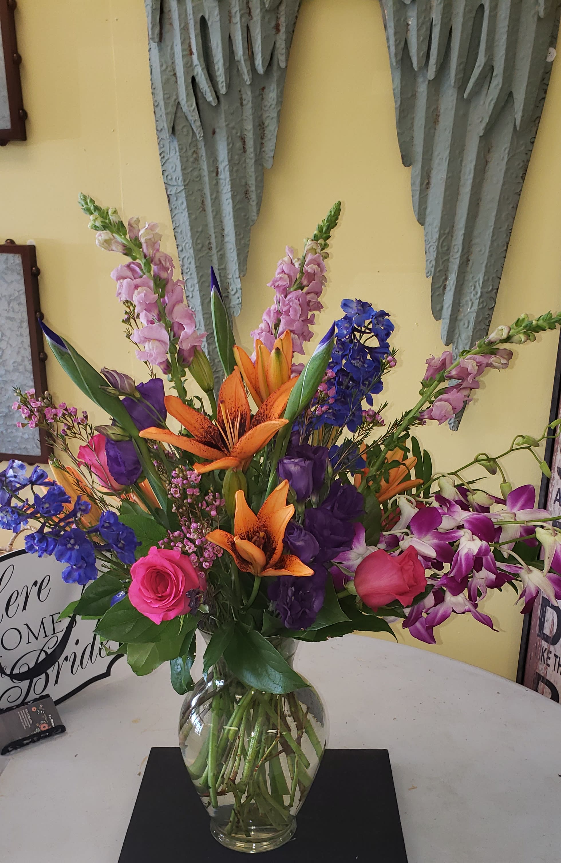 Colors Galore - This beautiful arrangement is full of vibrant colors and fun lilies, snap dragons, blue delphinium and orchids to add that extra flare.  
