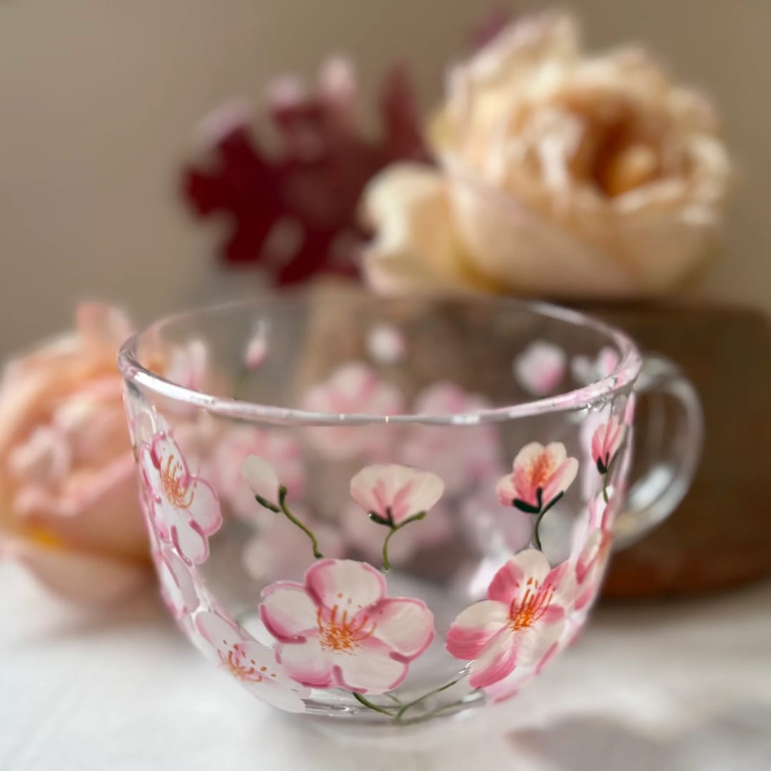 Painted Cherry Blossom Mug - The lifelike and vibrant cherry blossom design is carefully detailed, showcasing shades of pink and white, creating a stunning impression of natural beauty. The entire surface of the mug is covered in cherry blossoms, making it a perfect addition to any glassware collection.  The sturdy handle of the glass mug is designed for a comfortable grip, making it ideal for both hot and cold drinks. These mugs are perfect for enjoying your morning coffee or tea.  13 oz mug / Not microwaveable / Hand wash only