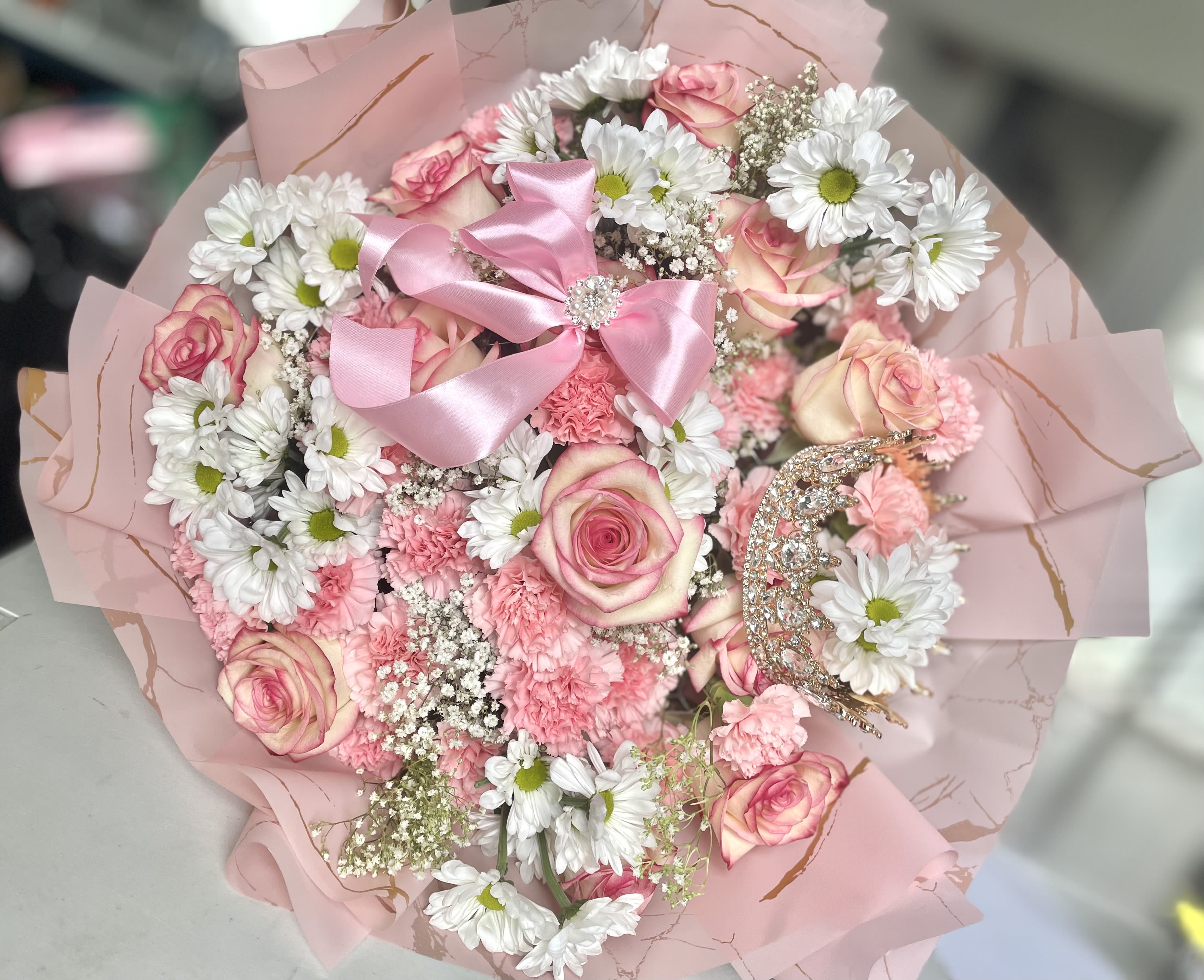 Blush Harmony - Delicate and graceful, Blush Harmony is a hand-wrapped bouquet in soft pink and white tones, blending roses, lisianthus, carnations, and seasonal fillers into a timeless arrangement. Nestled among the blooms is a sparkling rhinestone crown, adding a subtle touch of charm and elegance. Thoughtfully wrapped in natural paper and tied with satin ribbon, this bouquet is perfect for moments that call for beauty, warmth, and a hint of magic.