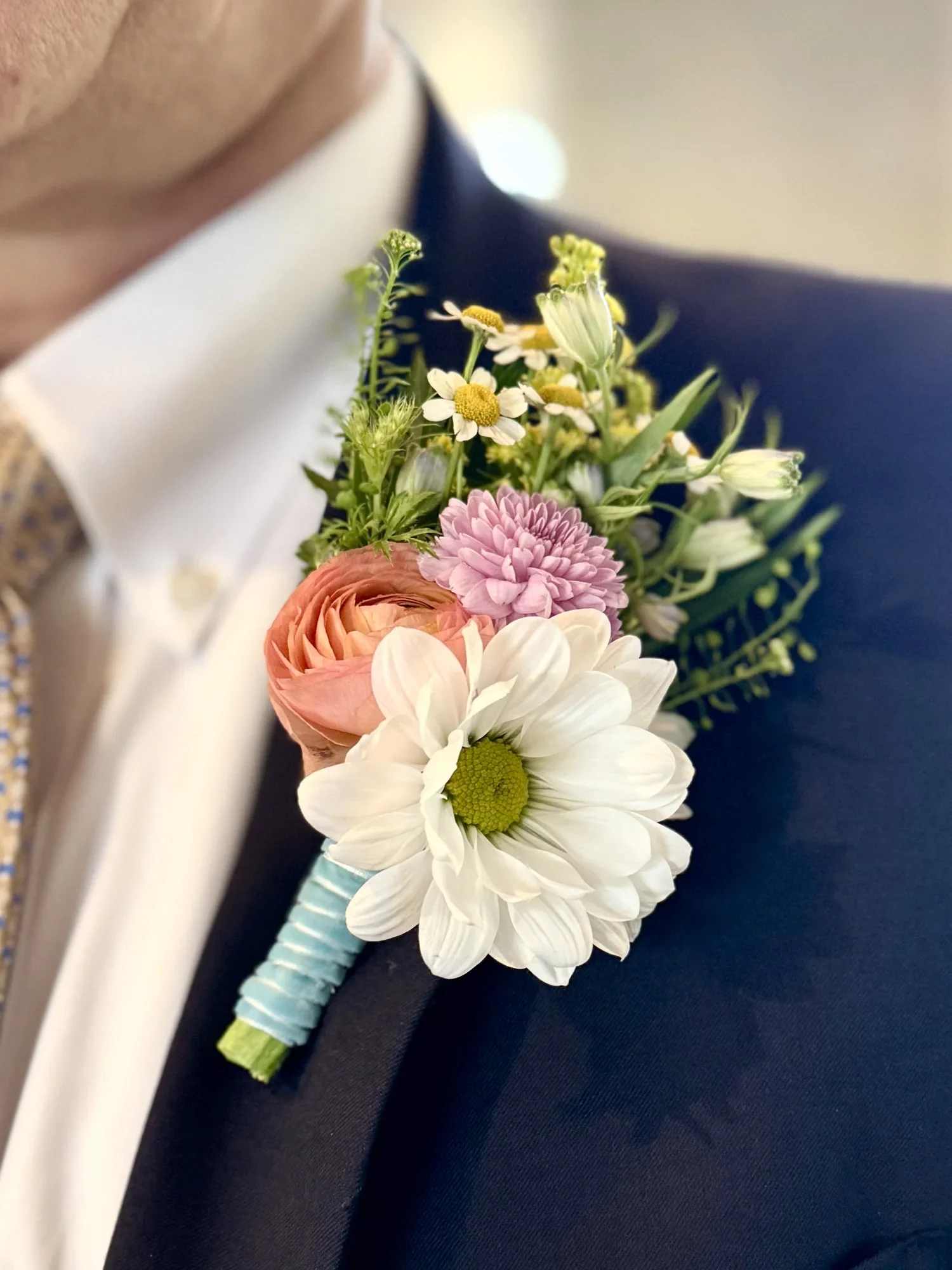 Lapel Boutonniere - A youthful and elegant design especially created by the Florist. Flowers are hand selected by the Florist. Perfect for weddings, prom, homecoming, and school dance.  Please specify preferred color theme in the Florist Instructions when ordering. Colors can be in White, Pink, Blue, Lavender, Orange, Red, Yellow, Green or No Preference.  Boutonnieres are wrapped in ivory ribbon (as pictured).  We highly advise ordering at least 2 days in advance to ensure availability of supplies for the Color Selection.  If your event falls on a weekend, choose Friday delivery. Boutonniere will stay fresh for a few days if kept in a fridge. Delivered in a waterproof box with clear plastic lid.
