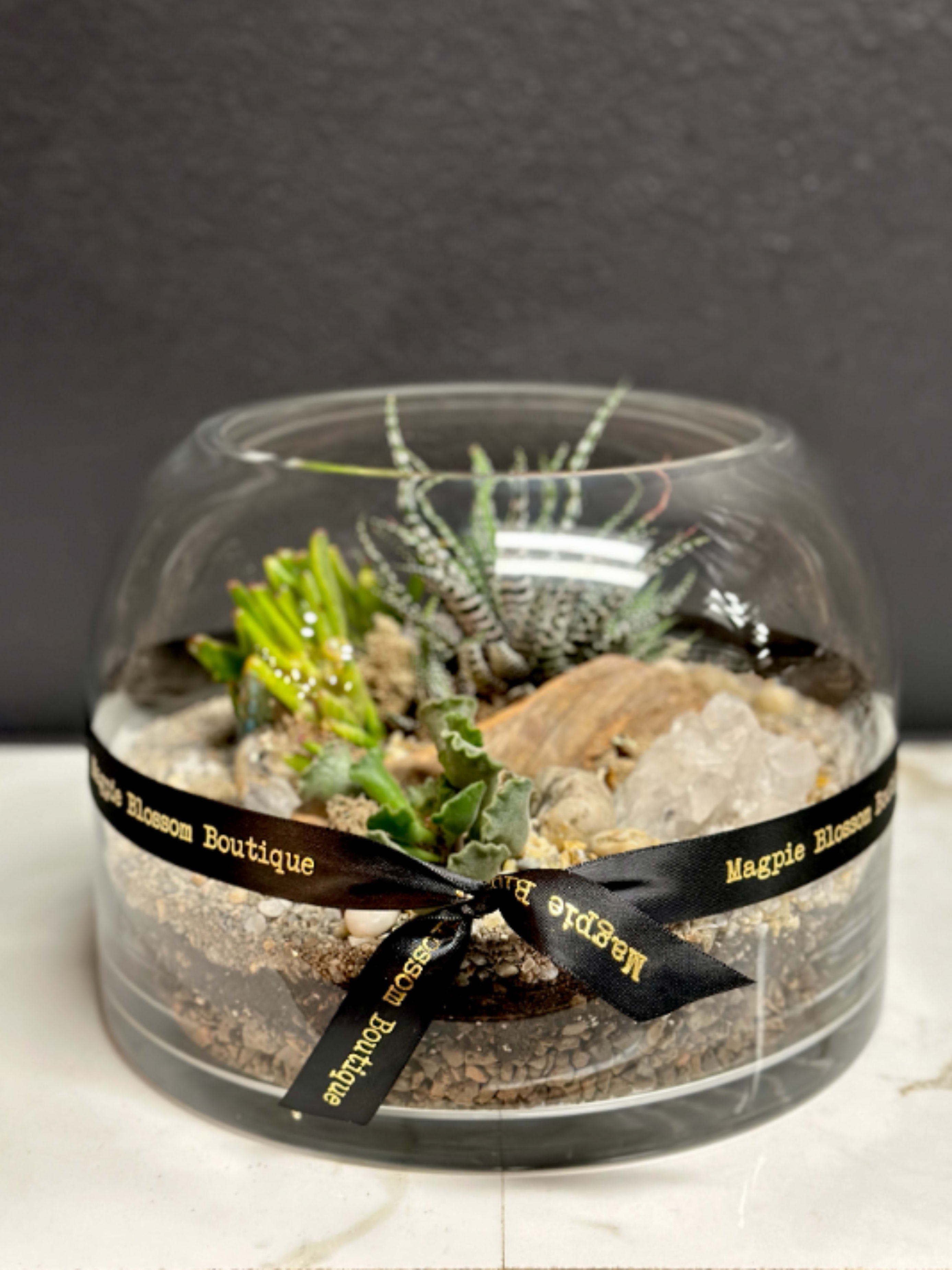 Rough Hollow Terrarium - Add a touch of nature to any space with our Rough Hollow terrarium. A stunning arrangemnt of succulents is enhanced with pebbles, crystals, &amp; natural accents.   Dimensions | Approximately 10x8