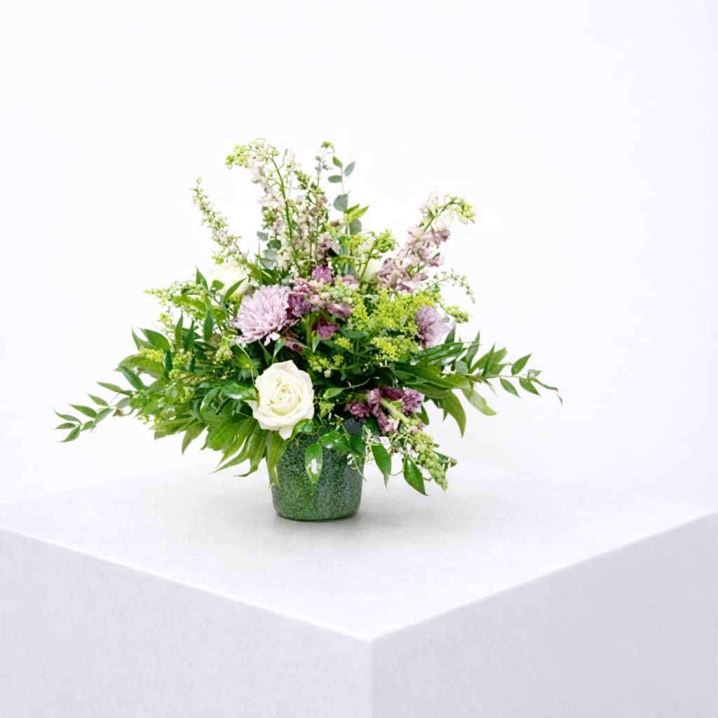 Strength and Silence  - Soft, graceful, and quietly powerful—Strength and Silence speaks volumes through its gentle beauty. Featuring serene tones of ivory, lavender, and fresh greens, this arrangement includes elegant roses, mums, snapdragons, solidago, and lush greenery thoughtfully arranged in a traditional mache basket.  Perfect for offering comfort during times of loss or quiet reflection, this piece conveys strength, peace, and heartfelt sympathy with every stem.
