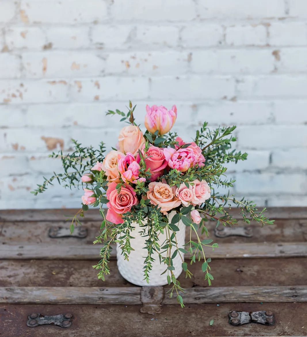 Pink and peach roses in a white vase with trailing greenery