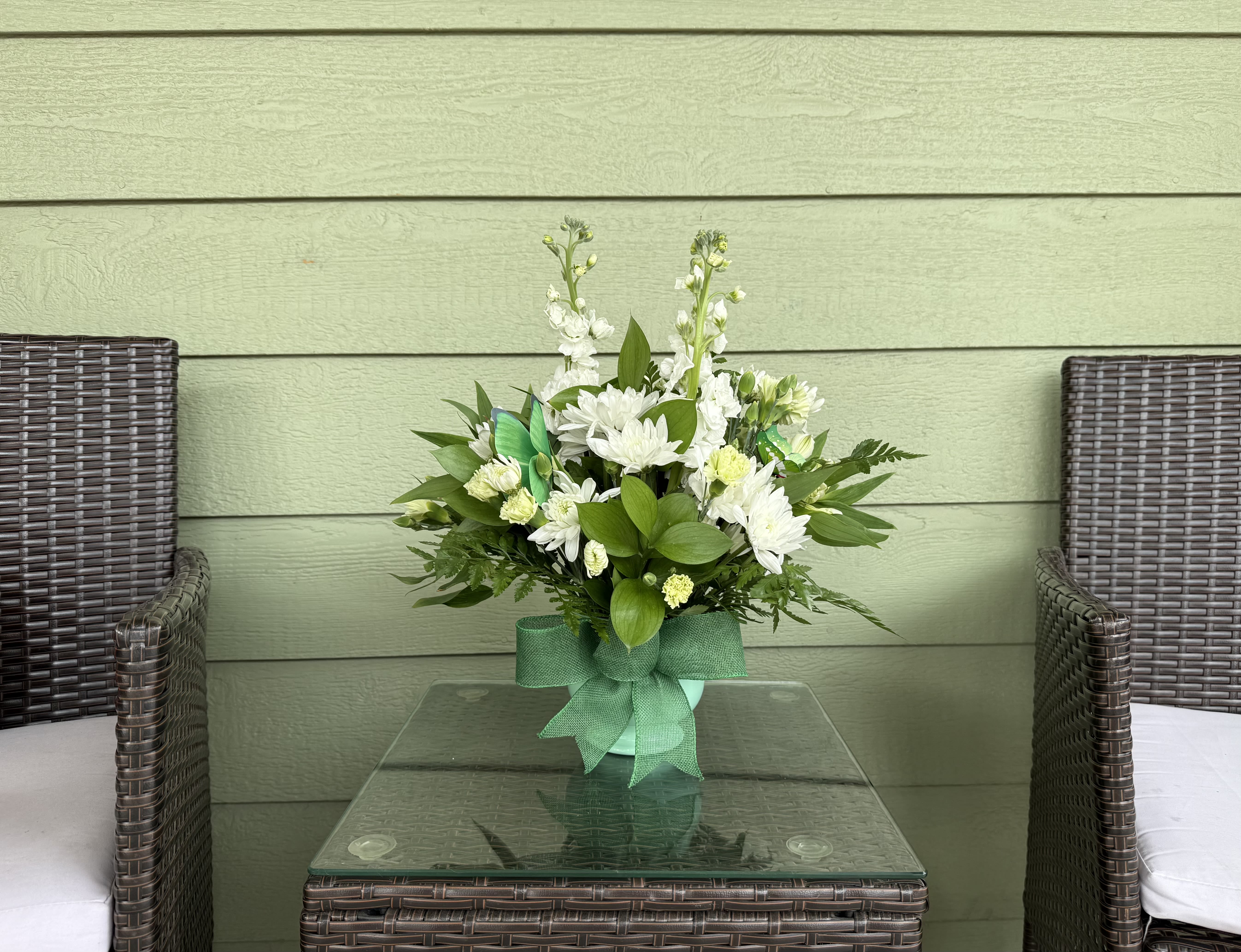 Irish Wish – St. Patrick’s Day Arrangement  - Celebrate the luck of the Irish with our Irish Wish floral arrangement. Designed in a charming green container with a festive ribbon, this fresh bouquet features elegant white blooms accented with lush green foliage for a classic St. Patrick’s Day look. Delicate snapdragons or stock, cheerful mums, and soft green carnations create a bright and uplifting design that feels both festive and sophisticated.  Perfect for sending a little luck, love, and Irish charm to friends, family, coworkers, or anyone who could use a smile this St. Patrick’s Day.   Occasions: St. Patrick’s Day, thinking of you, spring décor, thank you  Style: Fresh, festive, and cheerful  Approximate Size: 12–14” tall and 10–12” wide  Flower varieties may vary slightly based on seasonal availability while maintaining the overall look and feel.
