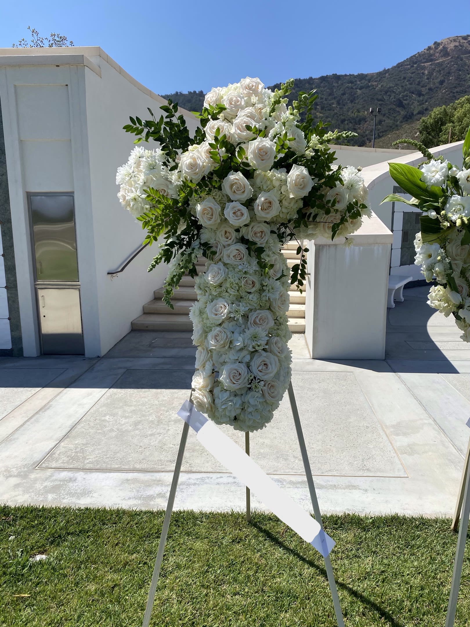 Heavenly Cross - Buzzy Bee Flowers - An all white tribute, this white cross funeral spray is pure and tranquil. Featuring a variety of white flowers, this elegant easel compliments the beauty of life.