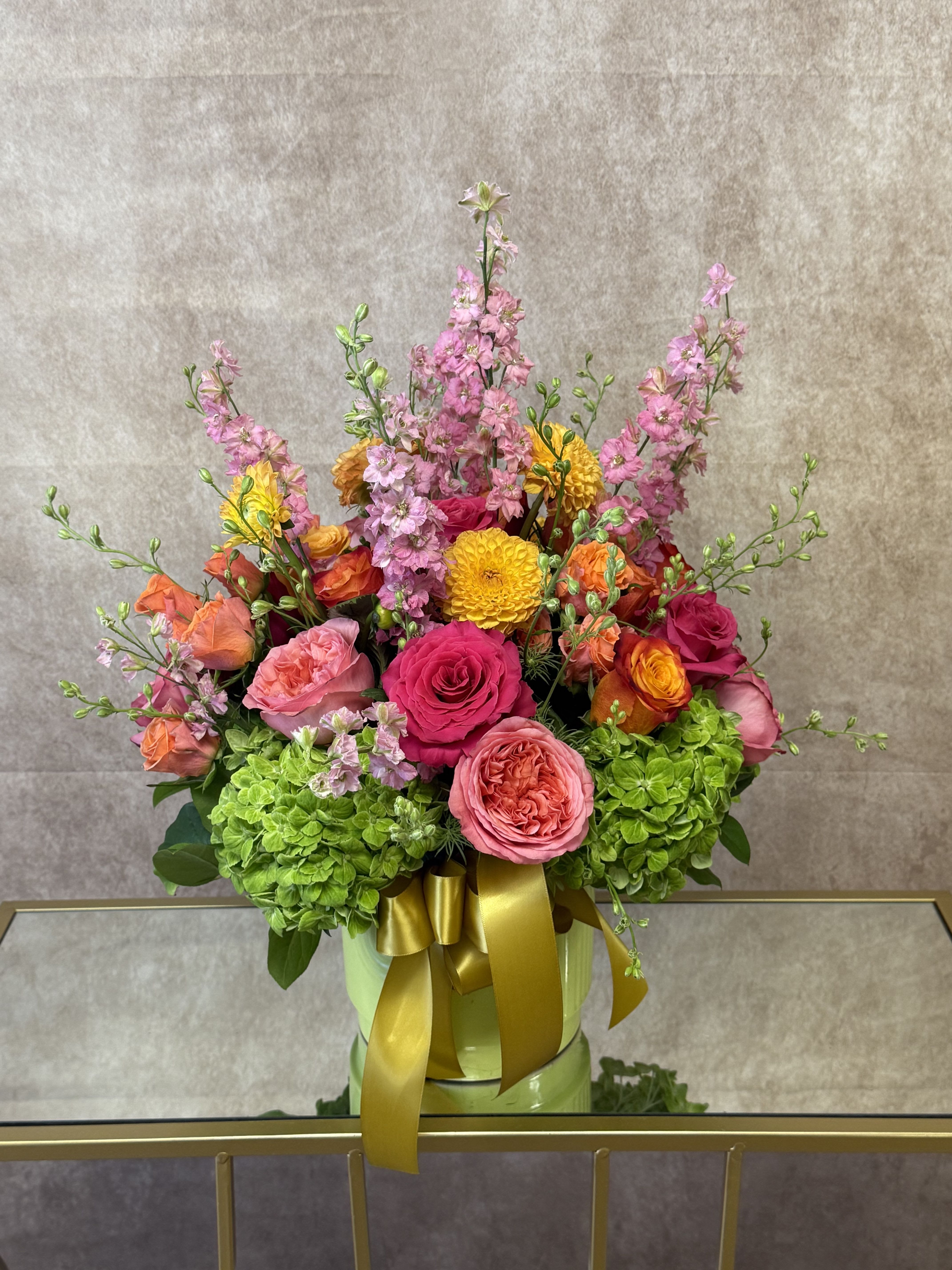 Bright Garden - Santa Clarita Valley Florist  - A vibrant, joyful burst of color, the Bright Garden arrangement is a celebration of nature’s most radiant blooms. At its heart, lush garden roses take center stage—their voluptuous, ruffled petals unfurling in shades of golden apricot, candy pink, and creamy blush, exuding a soft, honeyed fragrance.  