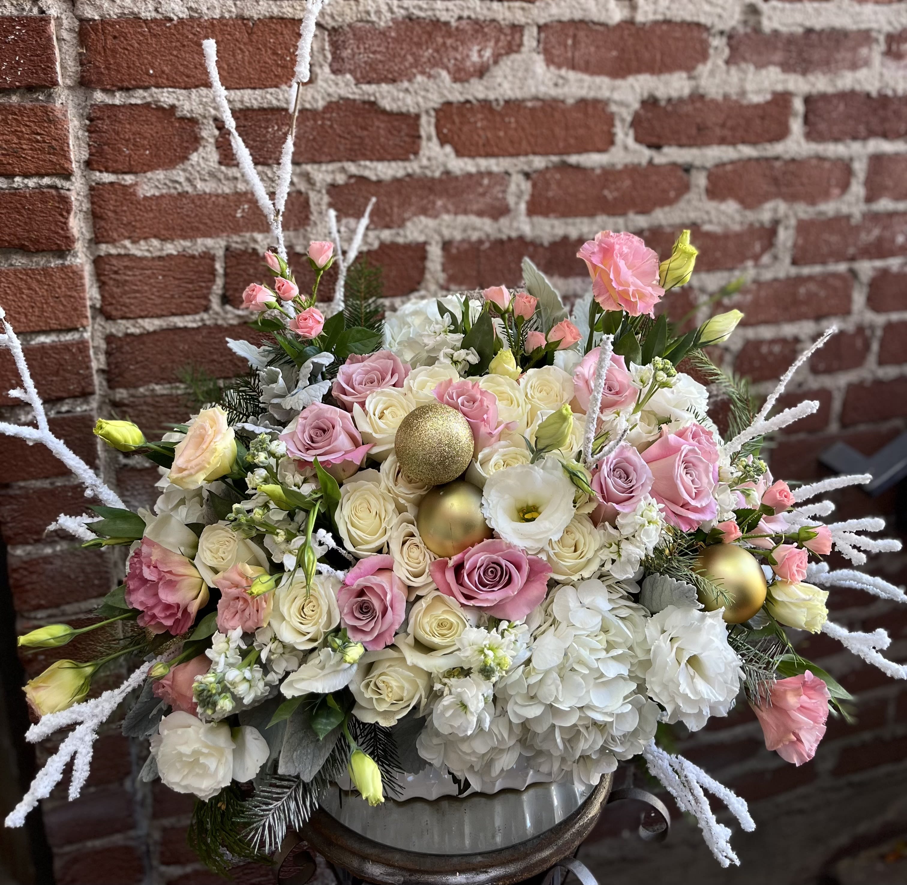 Jingle Bells - Buzzy Bee Flowers - Jingle Bells" is a whimsical and festive flower arrangement that embodies the lively spirit of the holiday season. This vibrant display is a symphony of colors, textures, and delightful elements reminiscent of the joyful sound of jingling bells.  At the heart of this arrangement, velvety red roses take center stage, mirroring the warmth and excitement of the season. Interspersed among the roses are sprigs of lush evergreen foliage, evoking the essence of a winter landscape. The rich greenery serves as the perfect canvas for an array of festive accents.
