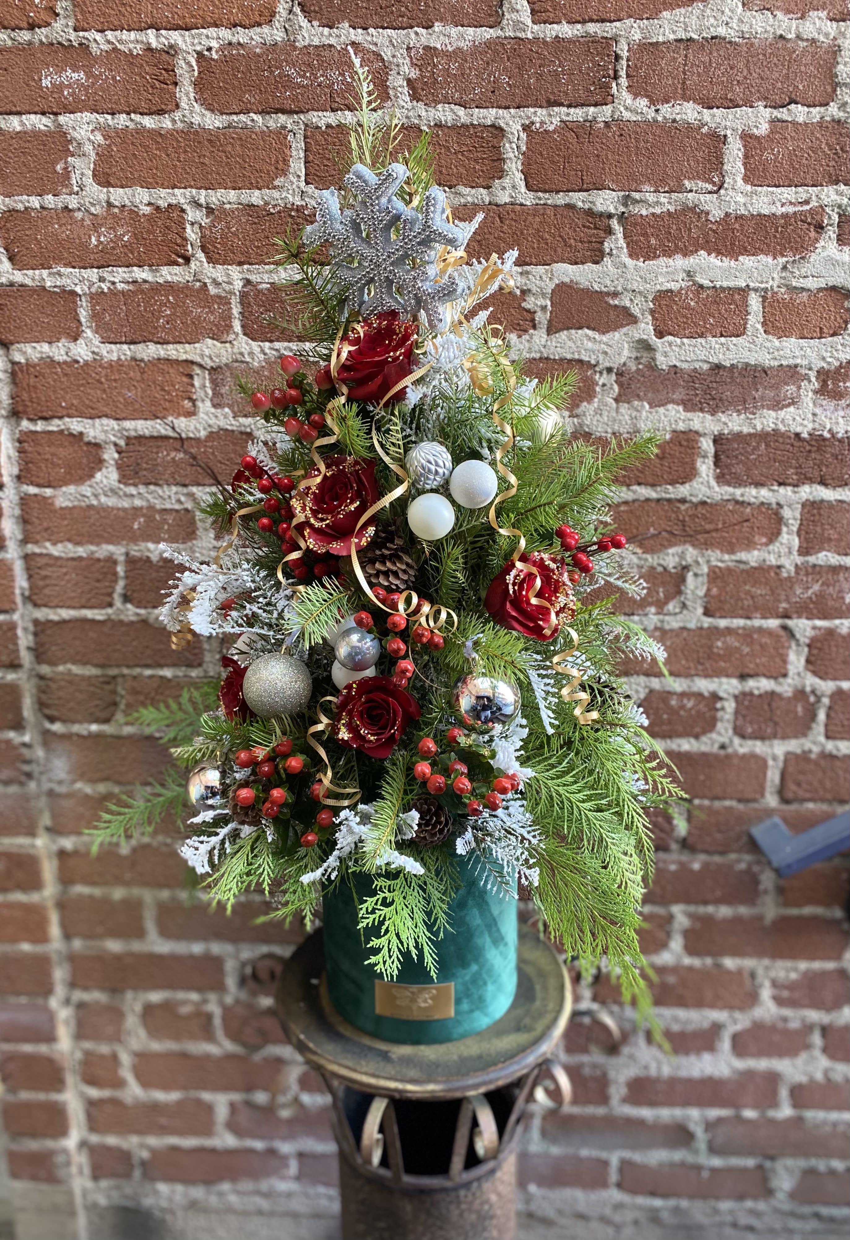 Oh Christmas Tree - Buzzy Bee Flowers - "Oh Christmas Tree" is a festive and enchanting flower arrangement that captures the spirit of the holiday season with its elegant and verdant design. The arrangement takes inspiration from the classic symbol of Christmas, the evergreen tree, and translates it into a breathtaking display of natural beauty.