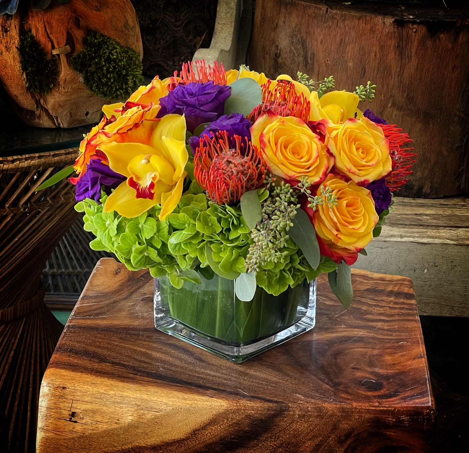 Bright bouquet of yellow roses, purple blooms, and orchids in a glass vase