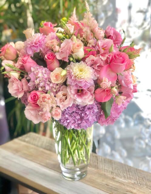 Mixed Boquet In Vase  - Vibrant and soft color pallet combination with assortment of blooms in tall glass vase. Coral Pink roses, spray roses adored with ranunculus, touches of lisianthus and stunning dahlias. Composition forms an outward style creating an organic freefall of florals.    Some florals are seasonal, if a particular flower will not be available due to season, we will substitute for similar flower, composition, color pallet and value of the arrangements as closely as possible. All effort to create a floral arrangement as close to the photo shown, the actual arrangement may vary slightly in its appearance from the photo shown. If you have any questions about your order, we welcome you to call us in or email    Available: Deluxe  Premium   Holiday Delivery:  Same-day delivery available. Deliveries are made throughout the day based on routing.