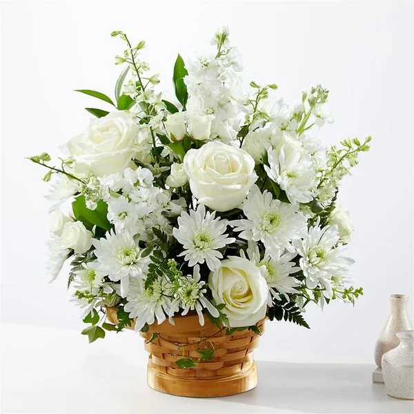White roses and mums arranged in a woven basket with soft white filler flowers