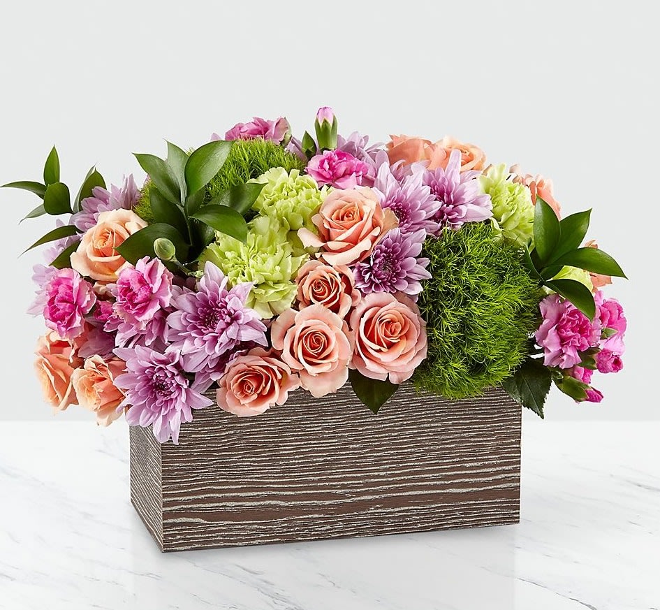 Simple Charm Bouquet - Capture the beauty of the seasons in bloom with our Simple Charm Bouquet. Gorgeous blooms such as peach spray roses, green trick dianthus, pink mini carnations and lavender cushion pompons fill a weathered wooden box with freshness. Whether you're saying thank you to a special friend or sharing the most heartfelt get-well message, this arrangement is a breathtaking gift for your loved ones to cherish. Color and shape of container may vary.