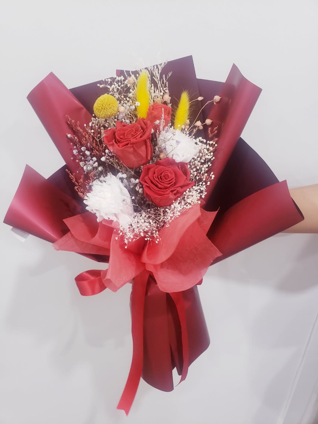 red rose &amp;white carnation preserved bouquet - 3 red preserved  roses and 2 white preserved carnations with yellow billy balls,bunny tails ,and baby's breath wrapped in bold burgundy and red korean-style papers.