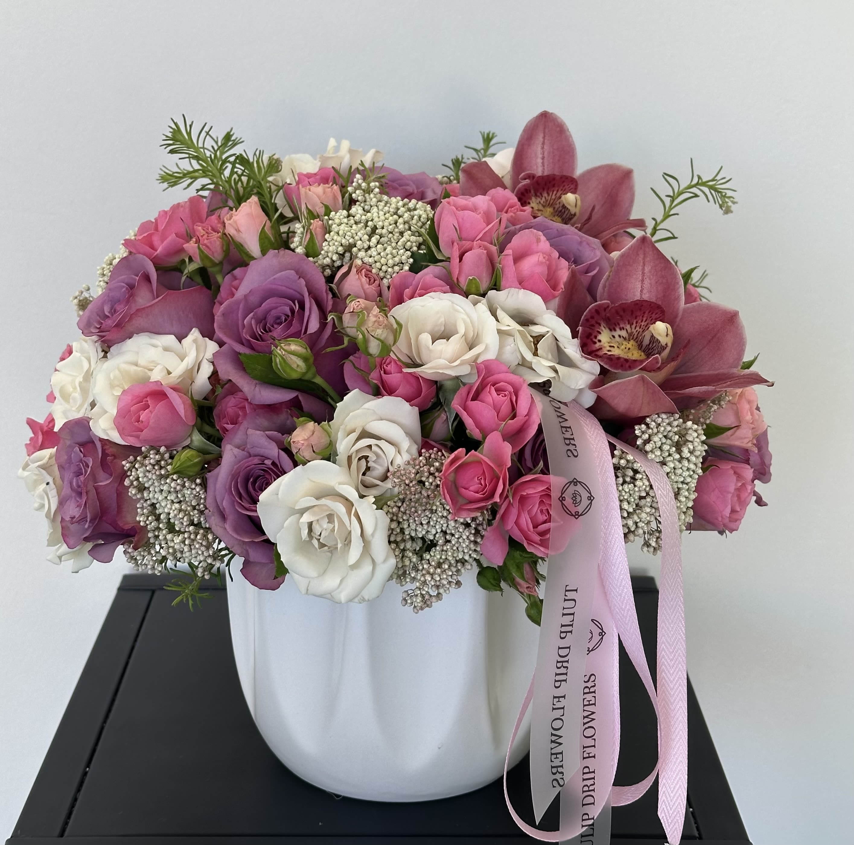 Anastasia Grace - A timeless composition of Roses, Spray Roses, Cymbidium Orchids, and delicate fillers arranged in a white ceramic vase. This elegant arrangement exudes romance and sophistication — perfect for birthdays, anniversaries, or special celebrations.