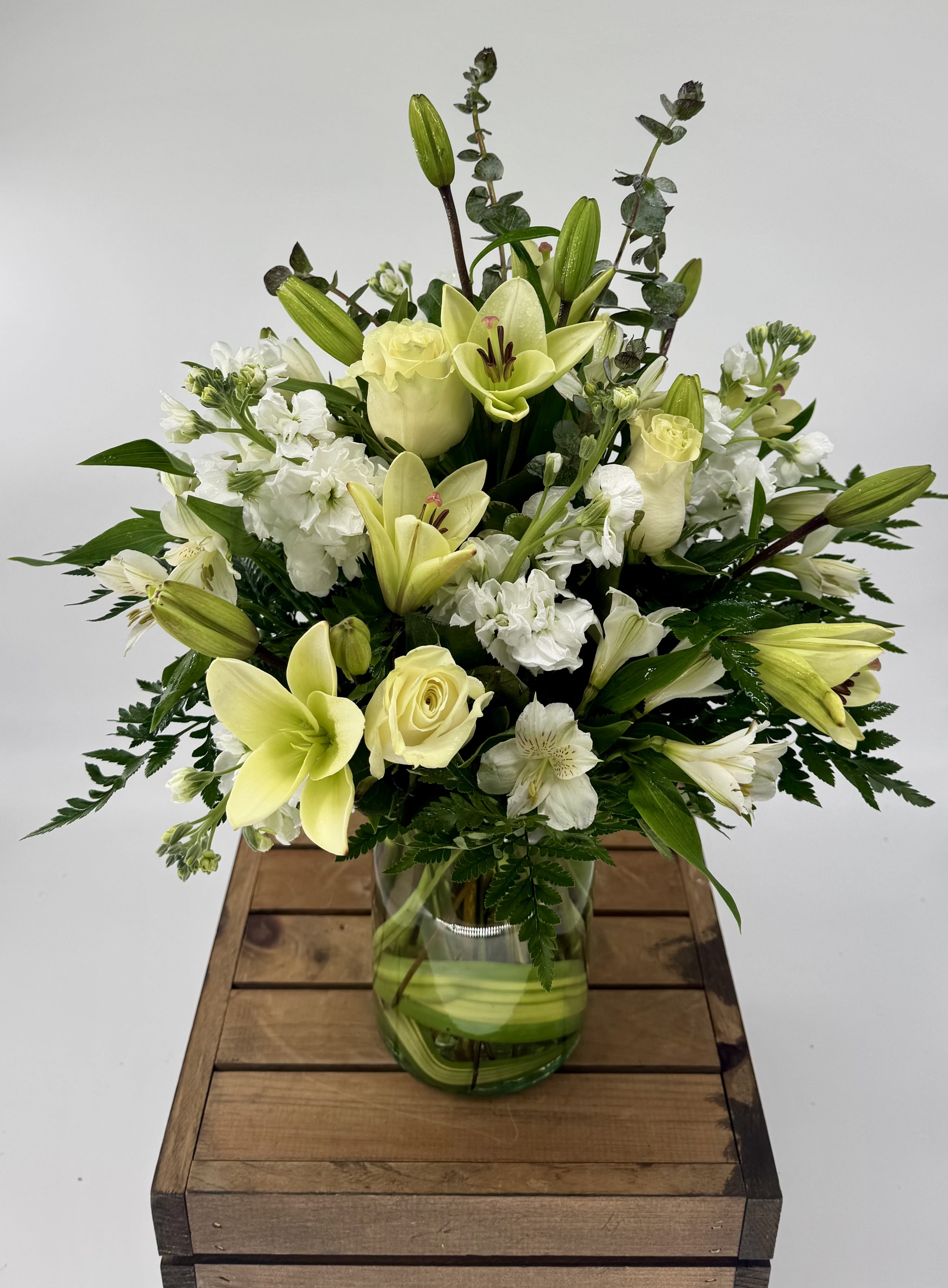 Eternal Rest (BR) - Introducing the "Eternal Rest" arrangement, a serene and heartfelt tribute to honor the memory of a loved one. This arrangement features a delicate combination of white roses, white lilies, white snapdragons, accompanied by lush greens and filler, all thoughtfully arranged in a clear glass vase.