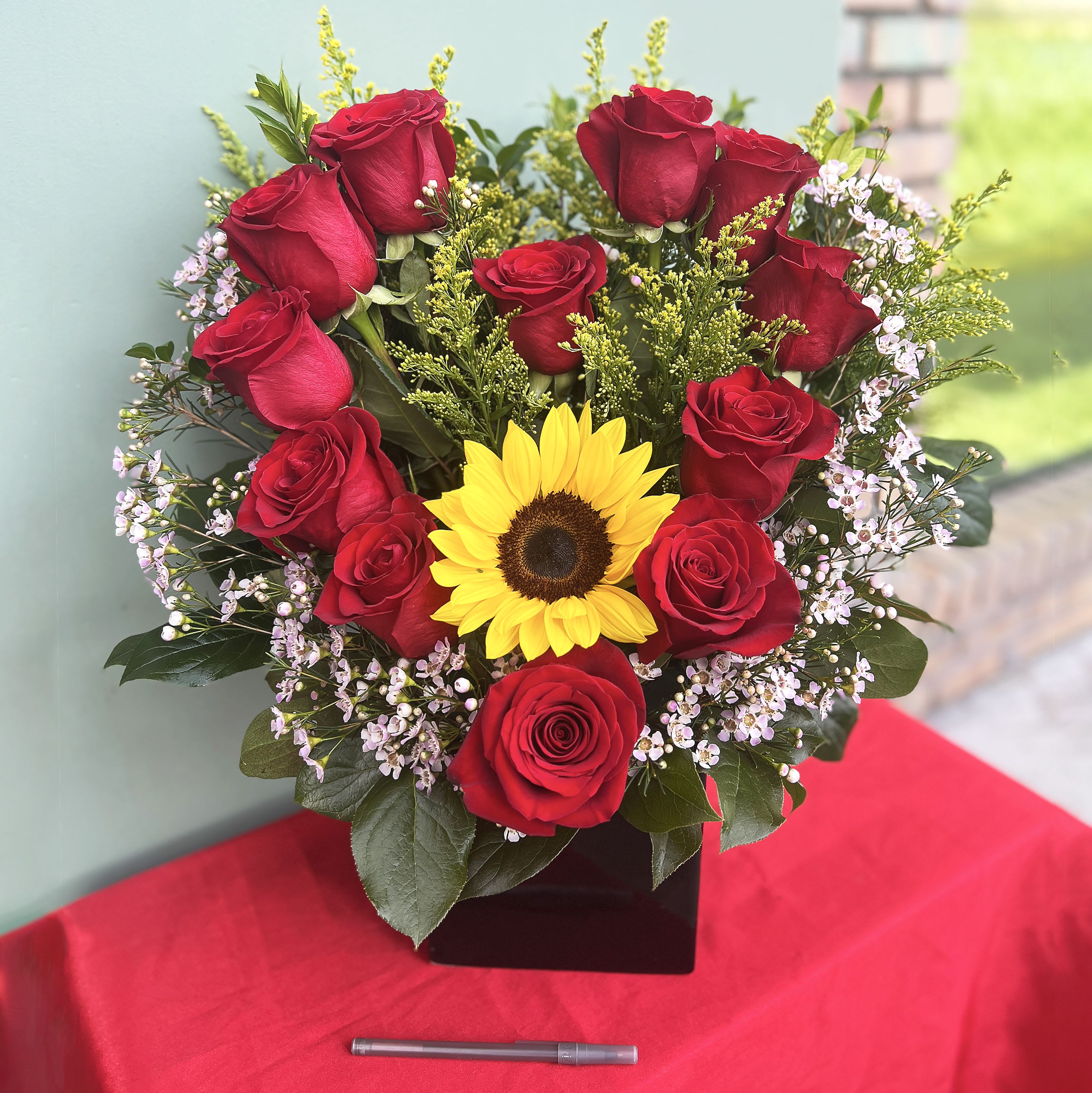 Heart So Bright - Heart So Bright is a romantic Valentine’s Day arrangement featuring a glowing sunflower embraced by velvety red roses and soft accent blooms. Symbolizing warmth, passion, and devoted love, this design captures the feeling of a heart shining at its brightest, bold, tender, and meant to be shared with someone truly special.