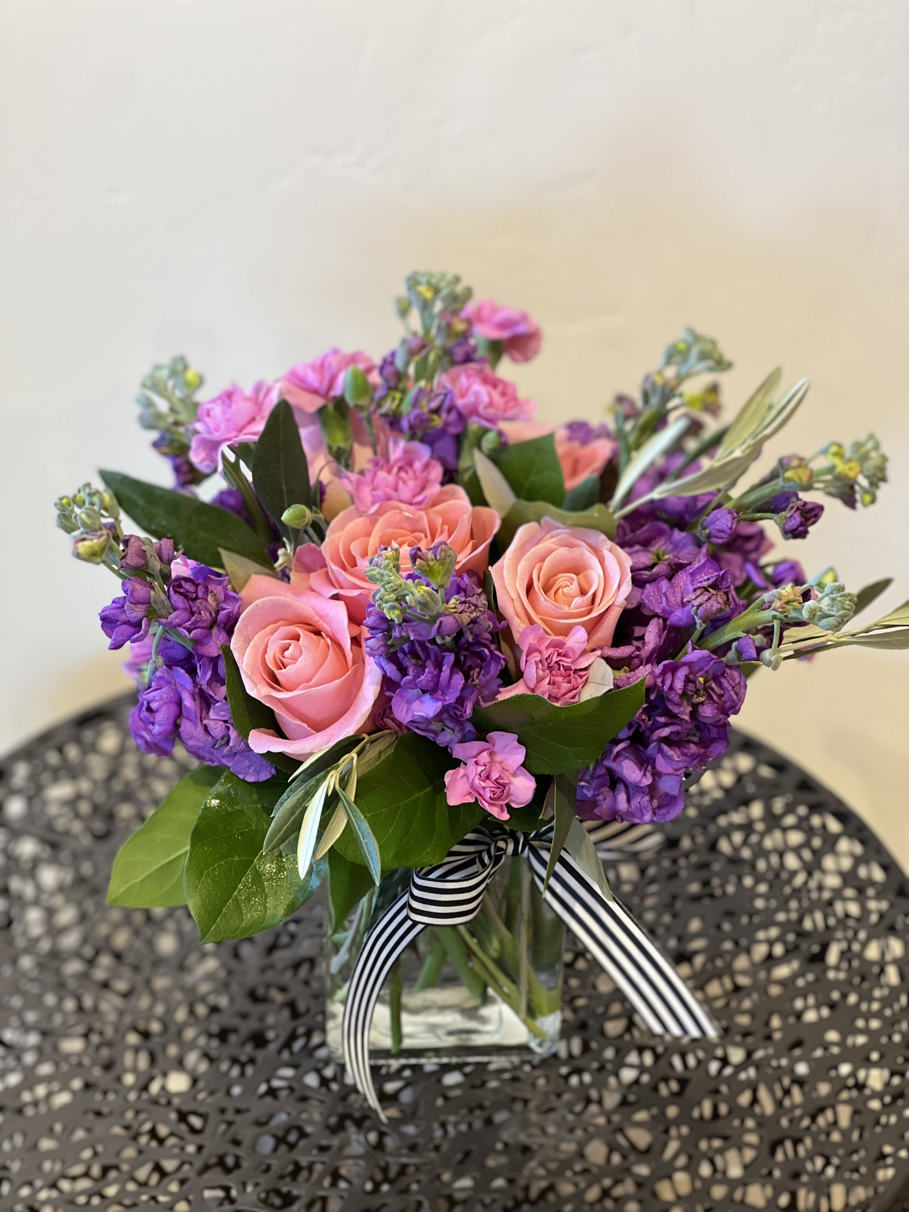 Sweetpea  - Sweetpea is designed with the perfect hue of bubble gum pink with a cream interior roses. Surrounded with purple stock and orchid pixie carns. All arranged in a glass vase, finished off with our signature ribbon. 