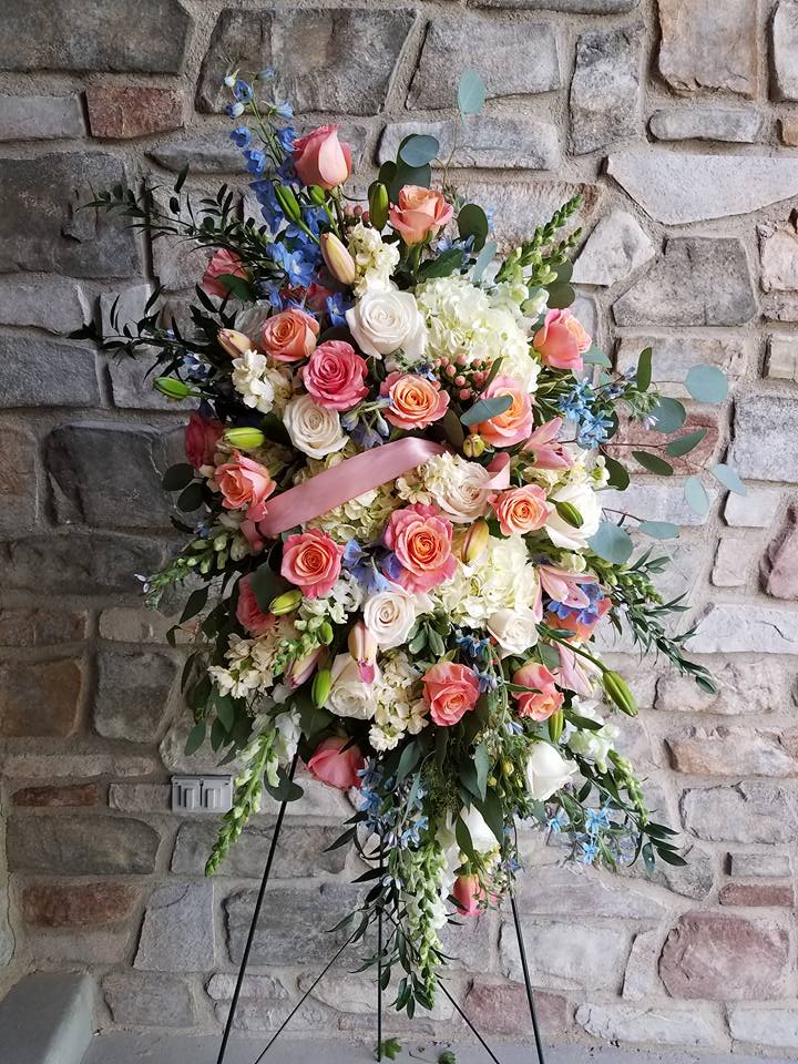 Serenity in Bloom Easel Spray by Simply Flowers - A gorgeous design filled with lush hydrangea, bi-colored roses, light blue delphinium, and seasonal foliage make up this beautiful tribute for the loss of a loved one. 