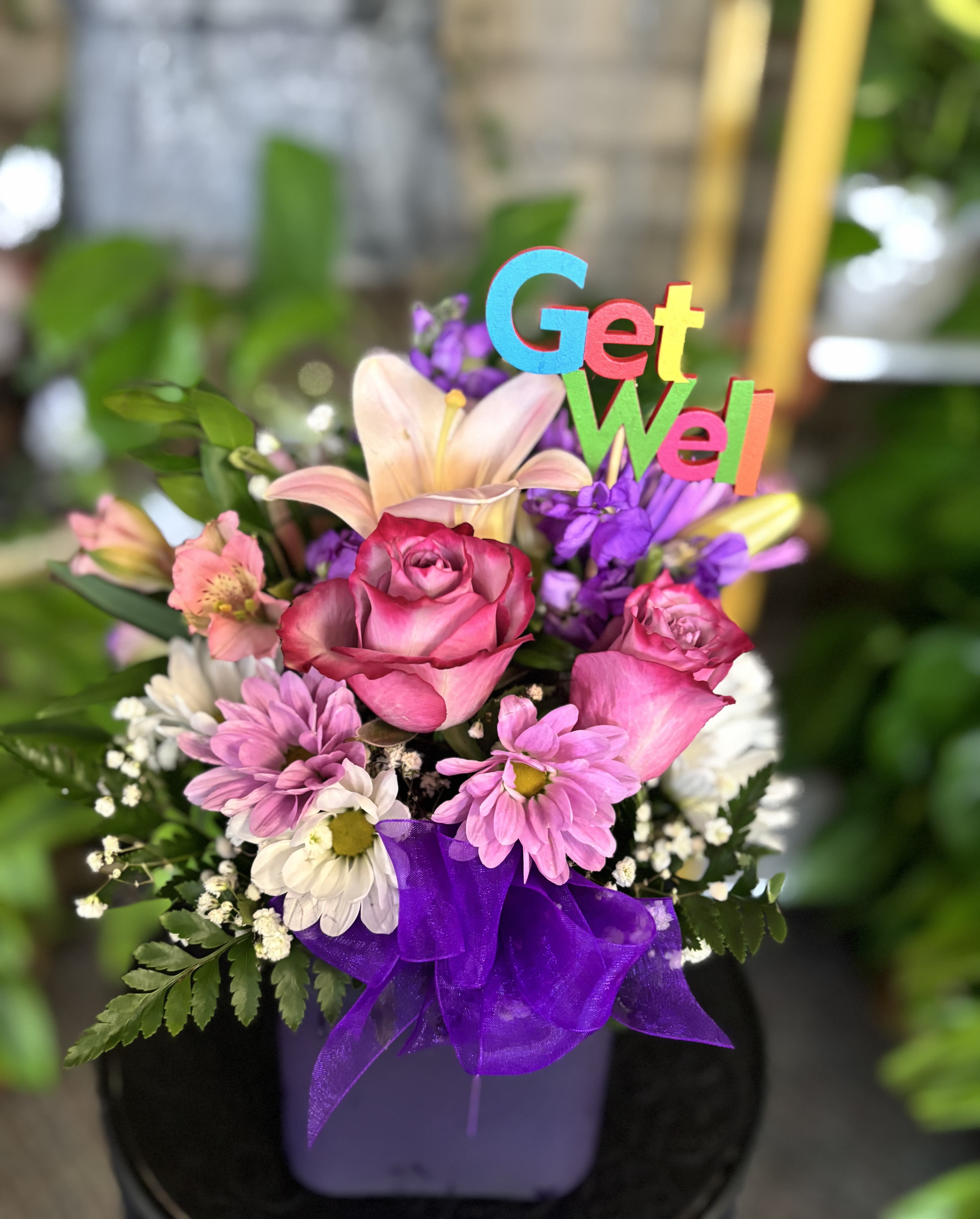 Pink roses and daisies in a purple container with a Get Well sign