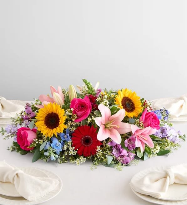 Painter’s Garden Centerpiece  -   Enliven any occasion with this wonderfully vibrant floral centerpiece. Hot pink roses, dazzling sunflowers, blue delphiniums (our 2026 Flower of the Year), and more blooms in a rainbow of hues help create a lively, welcoming ambience. 