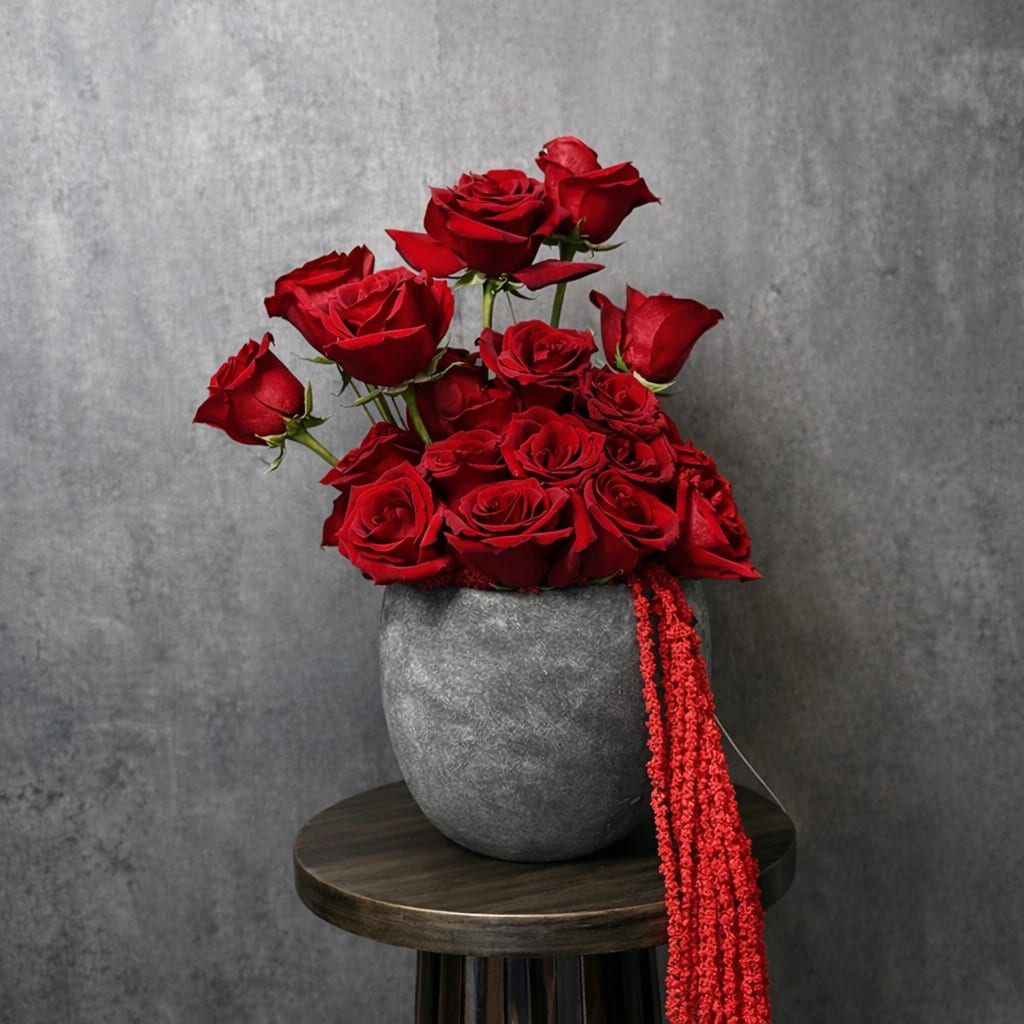 Red roses arranged in a gray vase with a red hanging ribbon