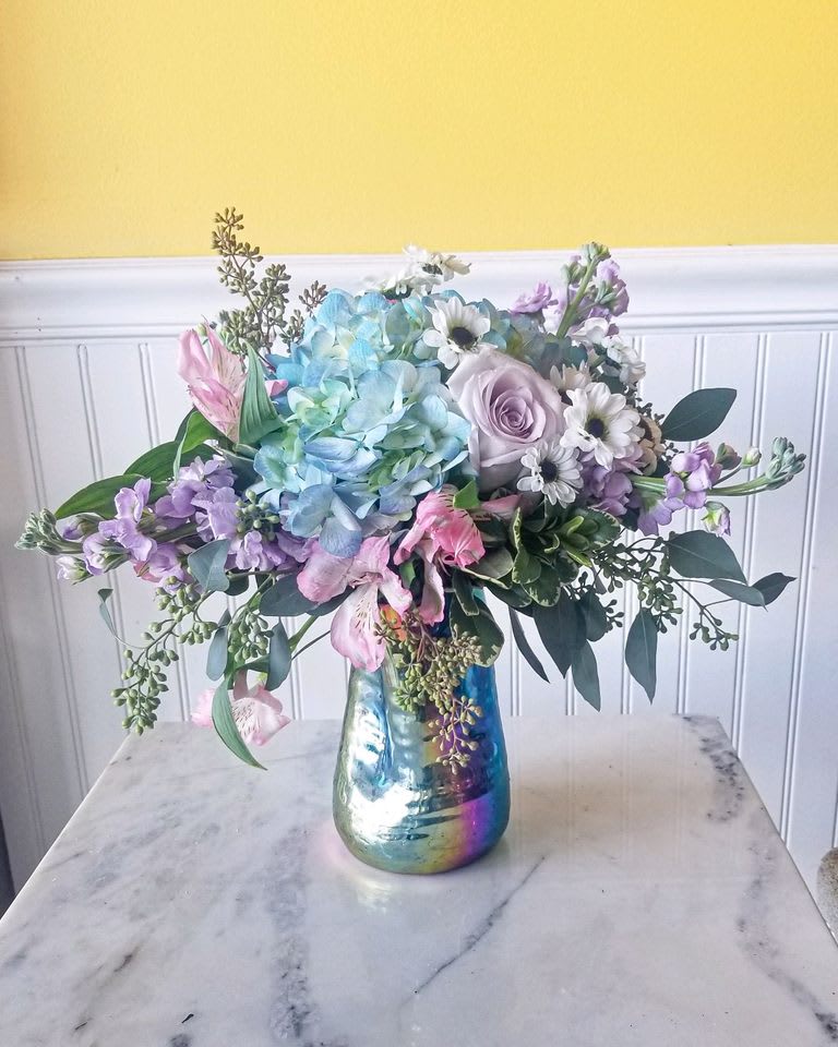 Carnival Candy - A uniquely shaped vase with light luscious flowers that smell and look good enough to eat .  But please don't really eat them ! The Vase is irregularly shaped and designed with an oil slick look, the flowers complement perfectly and will surly please the senses. dimension 13in X 12in