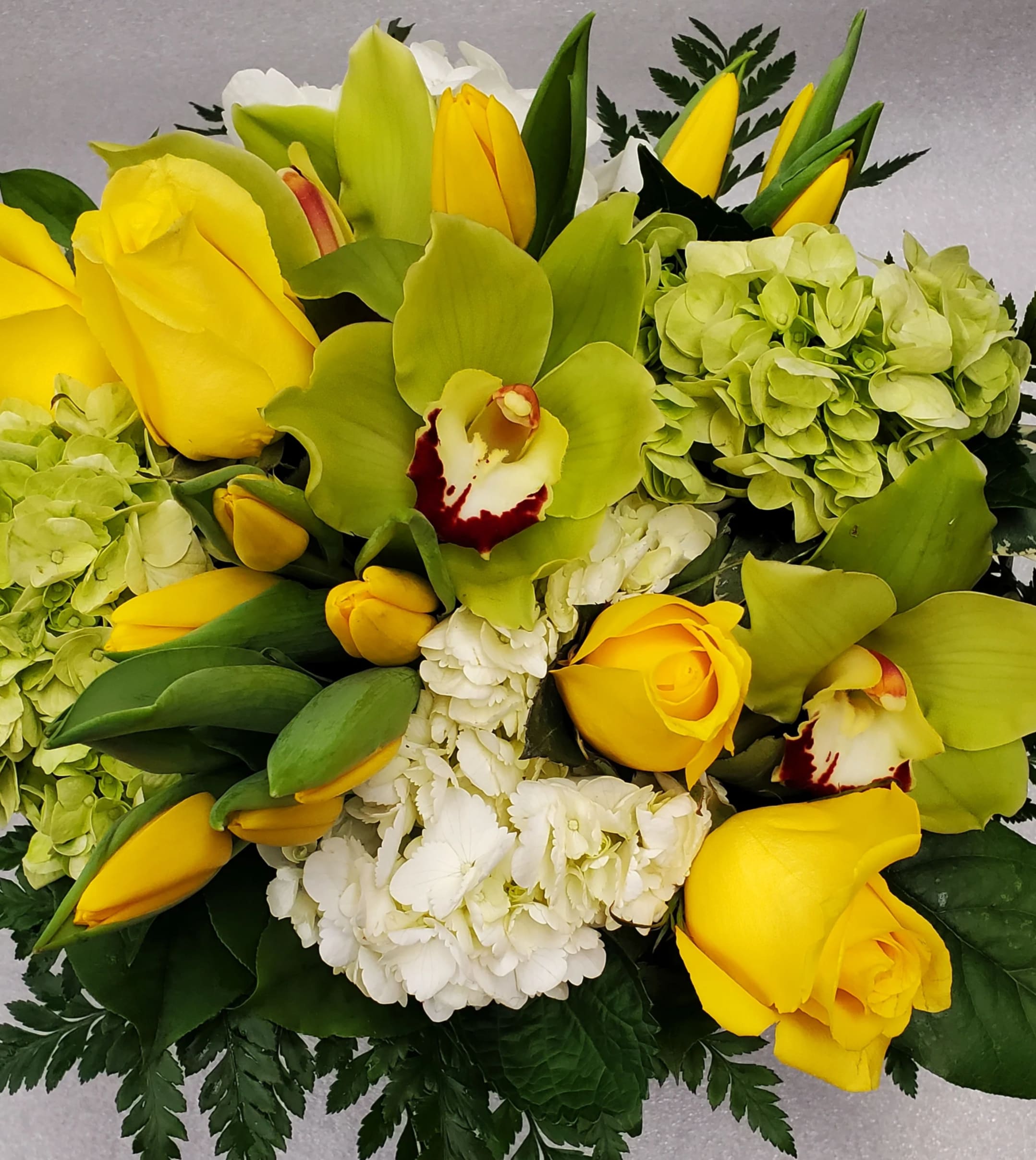 Citrus Sunshine - Bright yellows and greens designed in a  a low and lush arrangement with groupings of tulips and roses, accented with white and green hydrangea and cymbidium orchids. 
