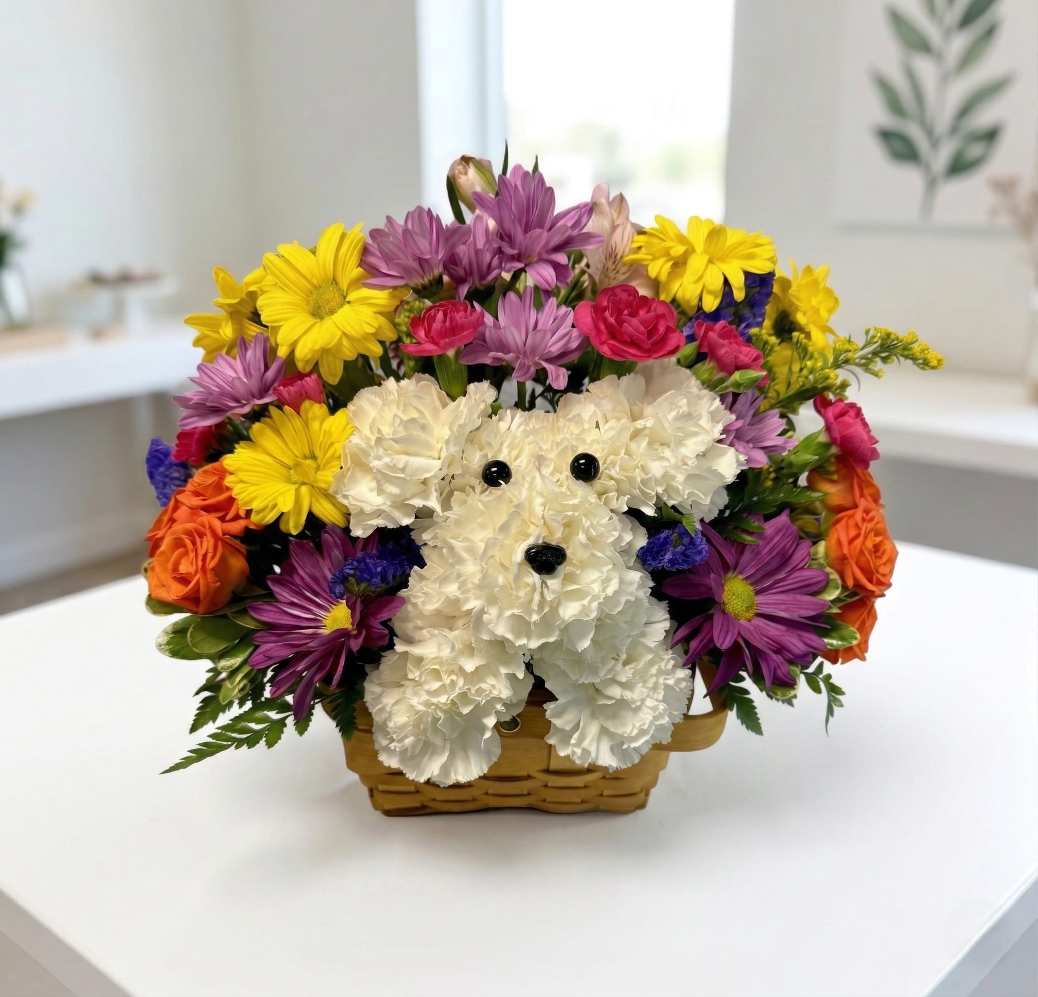 Fluffy the Pup - Bring a smile to someone’s face with our most charming floral creation yet! Expertly handcrafted by our Stone Oak designers, this whimsical arrangement features a delightful "puppy" sculpted entirely from fresh, creamy white carnations. Nestled in a vibrant garden of golden daisies, lavender poms, and petite spray roses, this playful pup is ready to deliver a huge dose of joy.  Finished with tiny button eyes and a nose, this unique centerpiece is perfect for:  Birthdays for the young (and young at heart!)  Get Well wishes to brighten a hospital room.  New Pet celebrations or "just because" gifts for dog lovers.  Each arrangement is tucked into a rustic basket, making it a "low-maintenance pet" that brings life and color to any home or office.