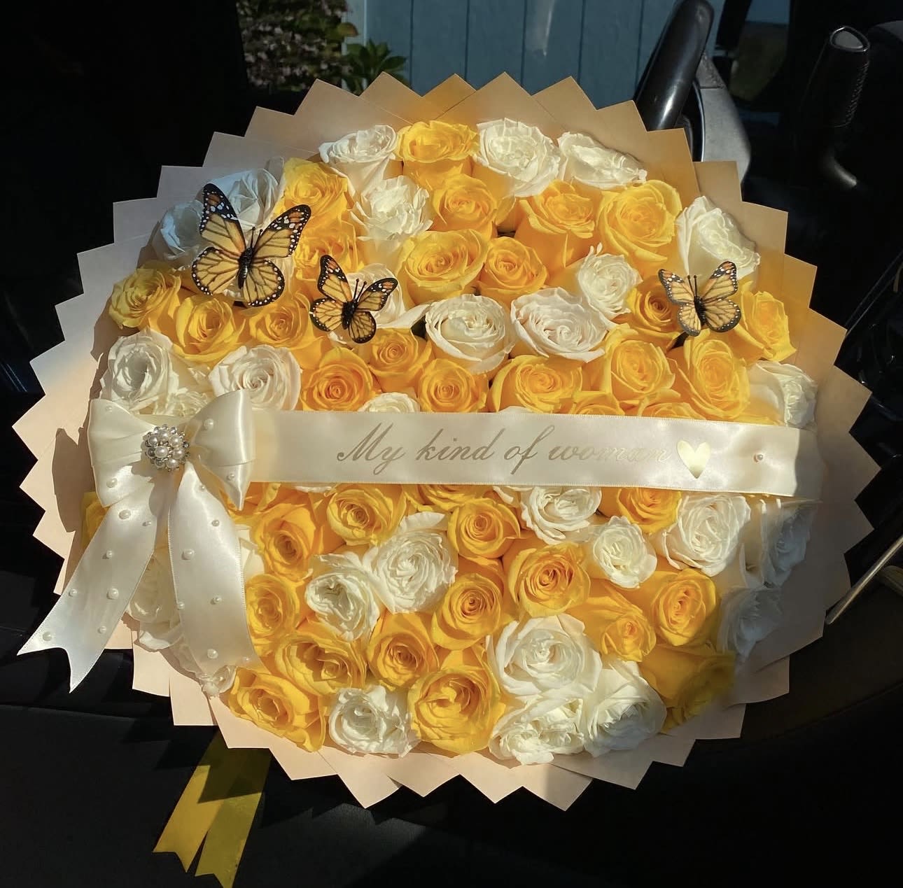 She is bright  - Make a breathtaking impression with this luxurious bouquet of radiant yellow and white roses, beautifully arranged in a full, rounded design. The vibrant yellow roses symbolize joy and admiration, while the elegant white roses represent purity and love, creating the perfect balance of beauty and meaning.  This stunning arrangement is wrapped in premium layered wrapping and finished with a delicate pearl-detailed bow and a romantic ribbon that reads “My kind of woman.” Decorative butterflies add a unique, charming touch that makes this bouquet truly unforgettable.  Perfect for anniversaries, birthdays, romantic surprises, or celebrating someone special, this bouquet is designed to turn heads and make the recipient feel truly cherished.