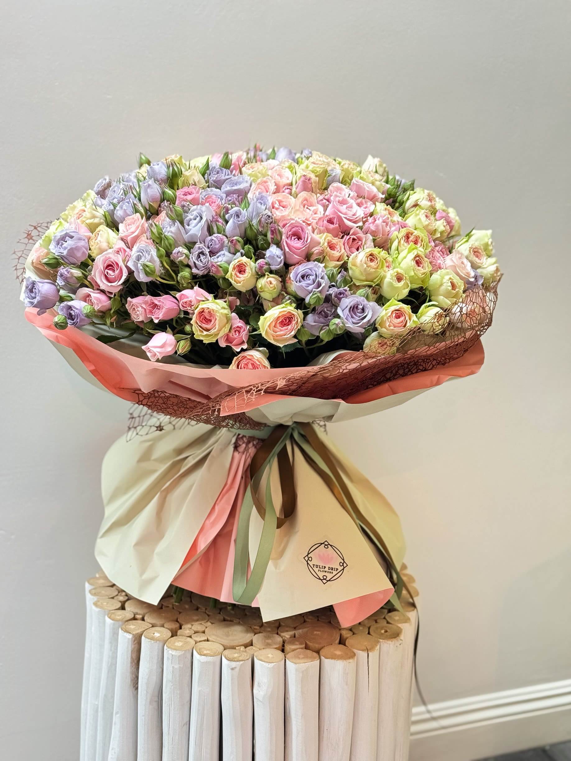 Large bouquet of pastel pink and lavender roses wrapped in cream and pink paper