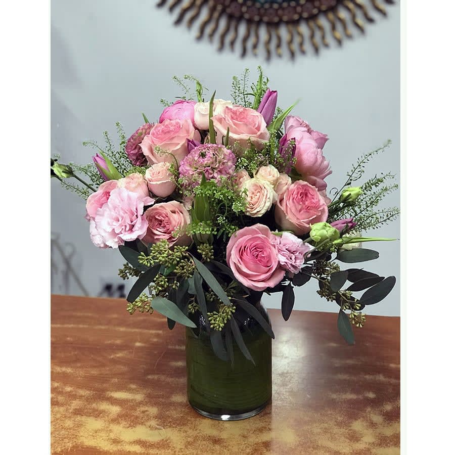 Emma's Song - A feminine and friendly composition to make her blush! Various light tones of pink garden roses, spray roses, lisianthus, ranunculus, peonies, and tulips. The arrangement accentuated with greenery in a cylinder vase leaf-laced. (Note: Tulips and peonies are seasonal flowers. When not available we will substitute them with similar quality flowers)  