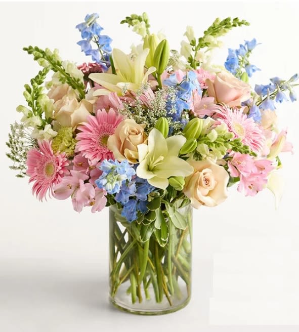 Delphinium Meadow arrangement  - pastel, our arrangement evokes the carefree joy of sauntering through a sun-dappled meadow in full bloom. Blue delphiniums, our 2026 Flower of the Year, mingle with sandy roses, pink Peruvian lilies, and more to create an irresistible gift.