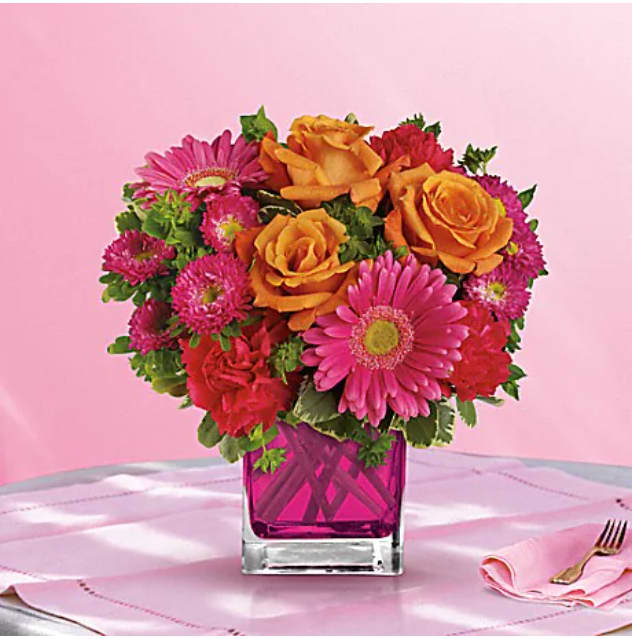 Turn Up The Pink Bouquet - Turn up the heat with this hot pink, haute couture creation! Super chic and oh-so-fun in its fuchsia Cube vase, this girly mix of gerberas and roses is sure to warm her heart. This brilliant bouquet of lush orange roses, hot pink gerberas, carnations and matsumoto asters are accented with bupleurum and variegated pittosporum. Delivered in a glass Cube. 